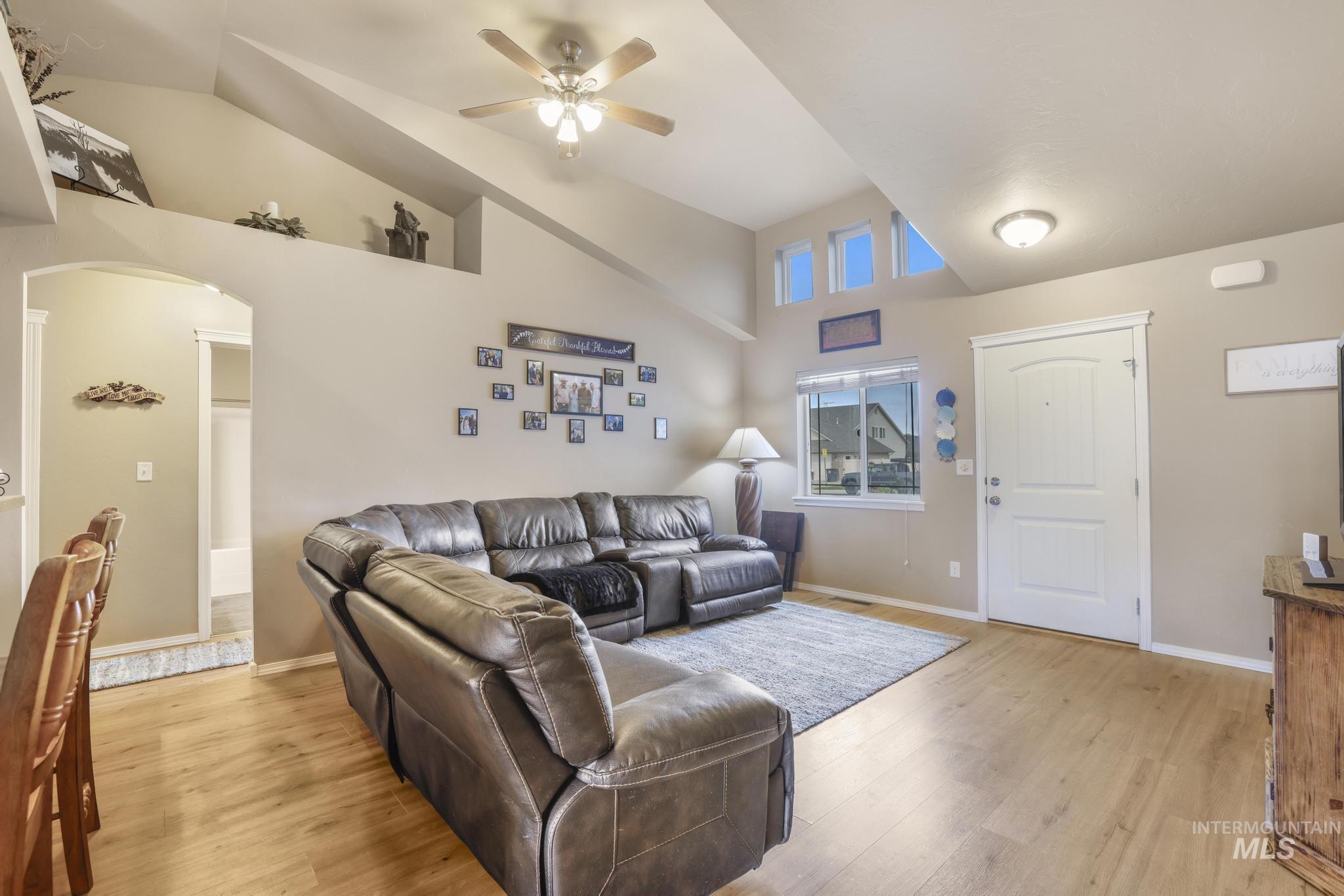 Living room featuring light wood finished floors, arched walkways, high vaulted ceiling, and a ceiling fan