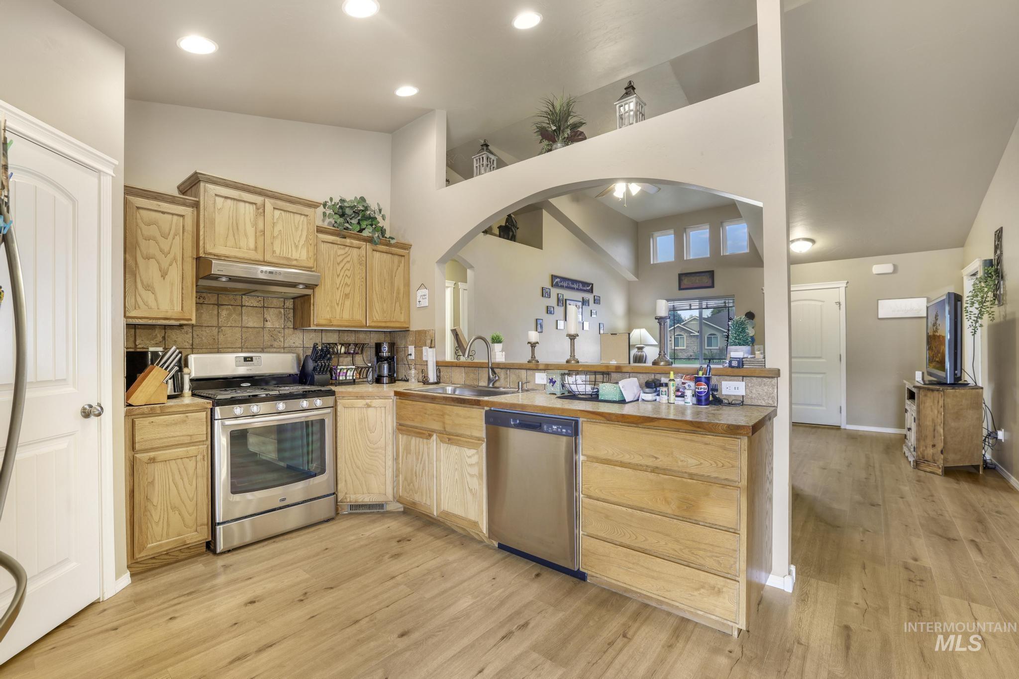 Kitchen featuring stainless steel appliances, arched walkways, decorative backsplash, light countertops, and a peninsula
