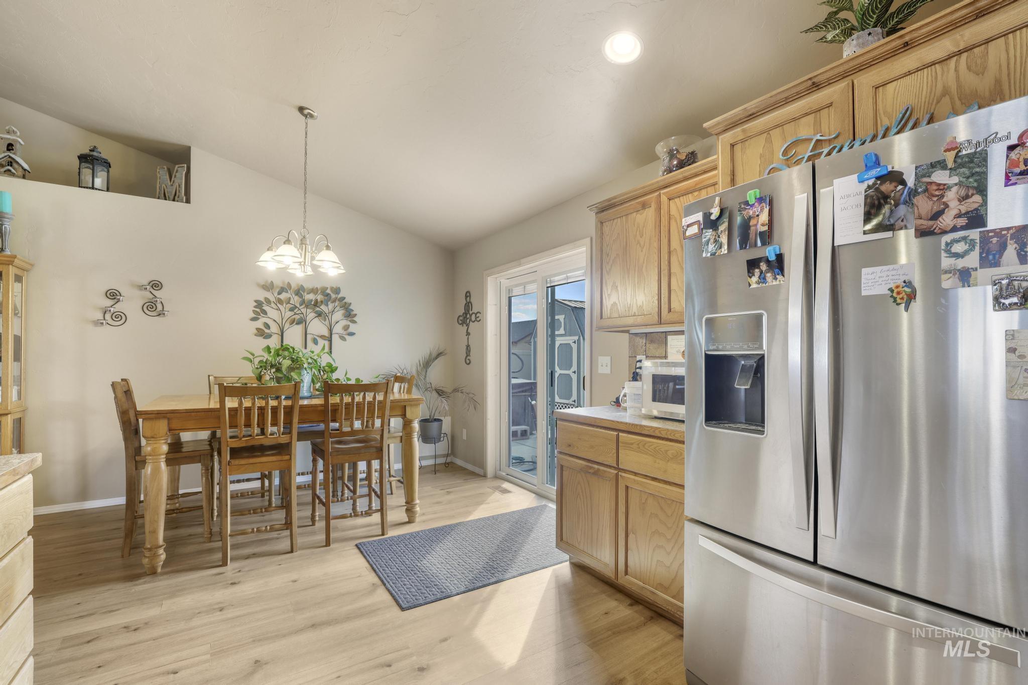 Kitchen with stainless steel fridge, lofted ceiling, light wood-style floors, light countertops, and hanging light fixtures