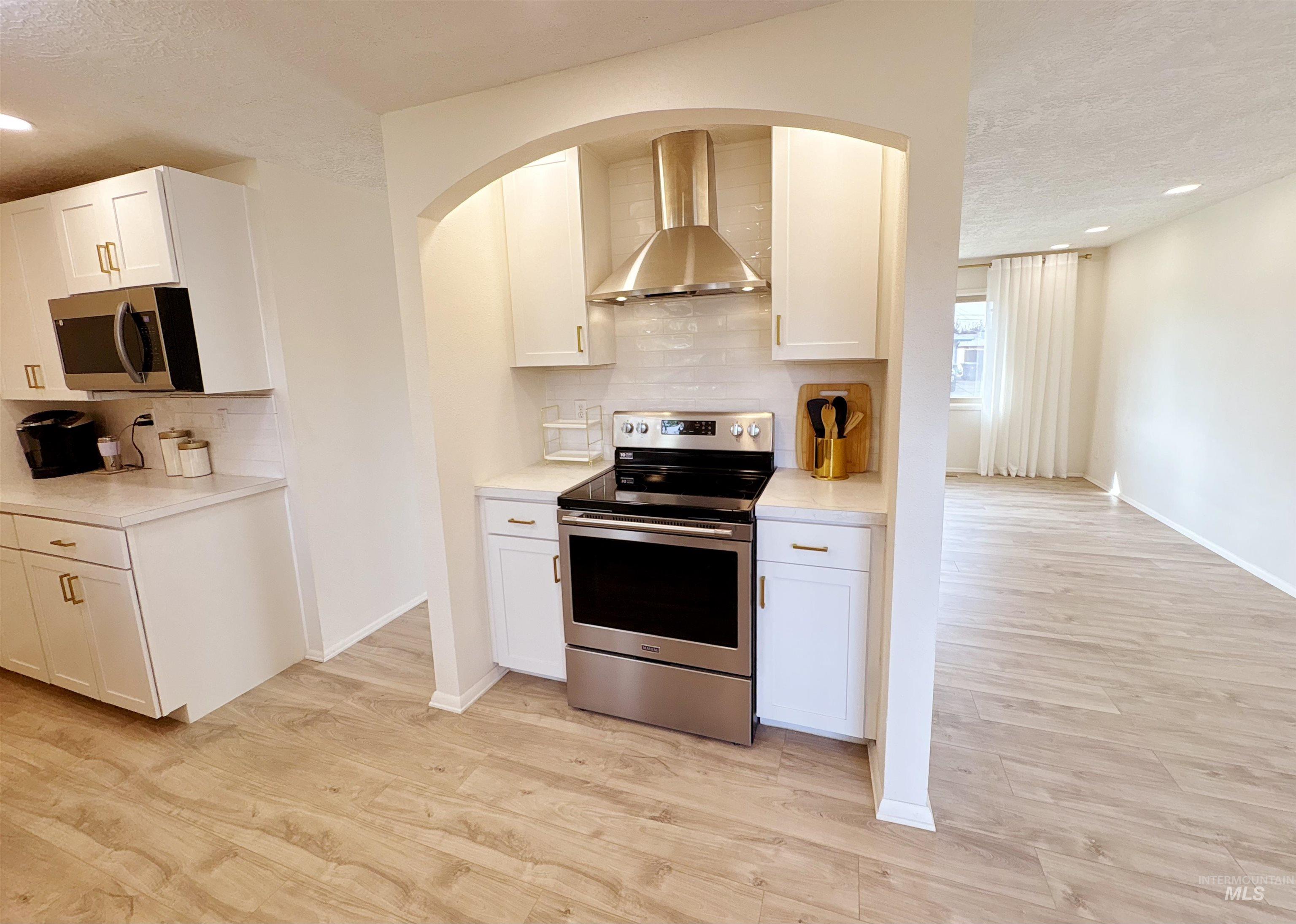 Kitchen with a textured ceiling, appliances with stainless steel finishes, extractor fan, backsplash, and recessed lighting
