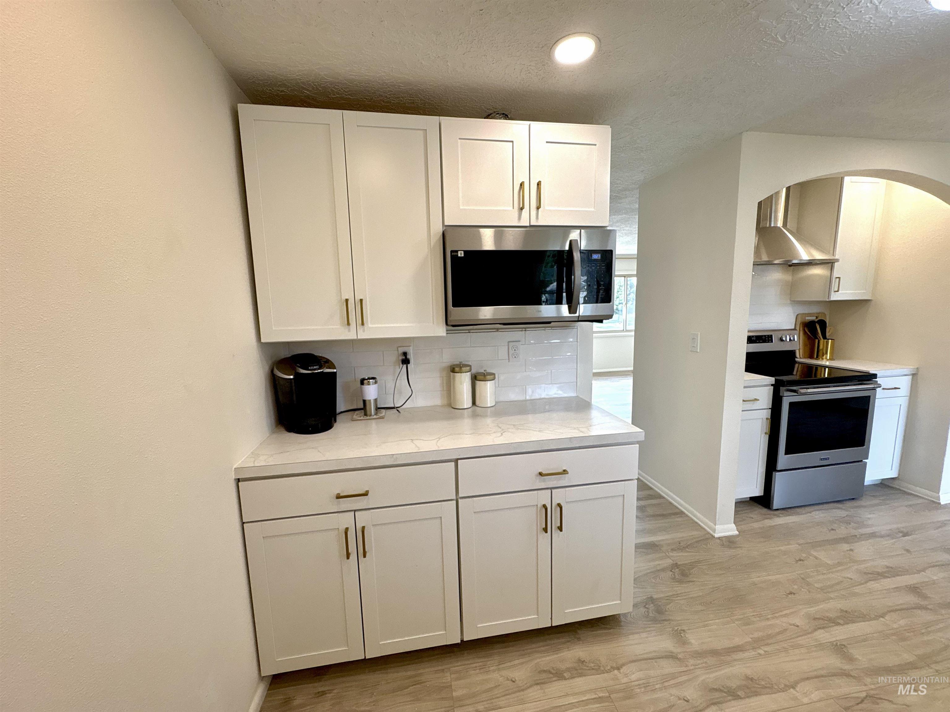Kitchen with appliances with stainless steel finishes, white cabinetry, light wood-type flooring, backsplash, and a textured ceiling
