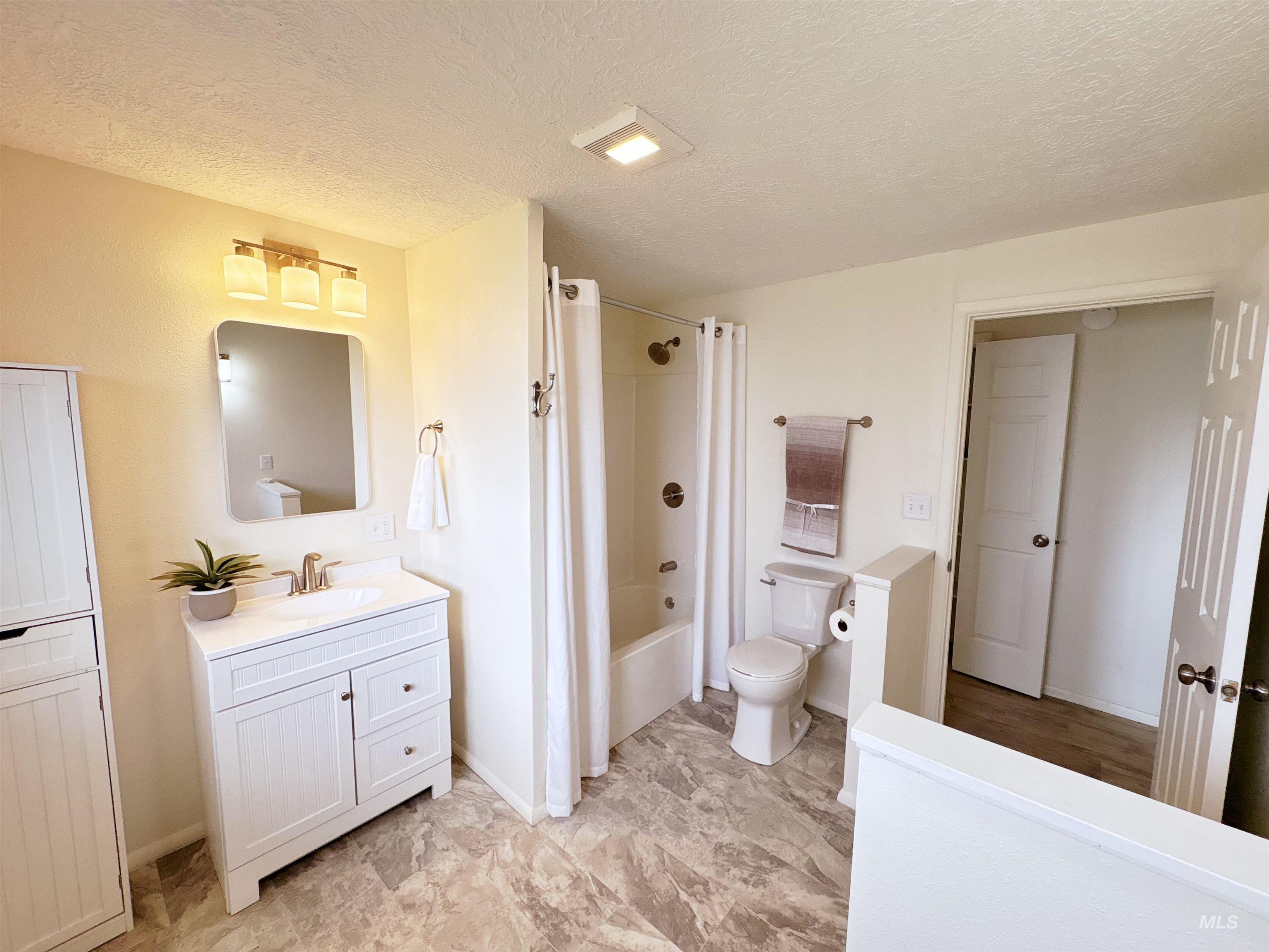 Bathroom with a textured ceiling, shower / tub combo with curtain, and vanity