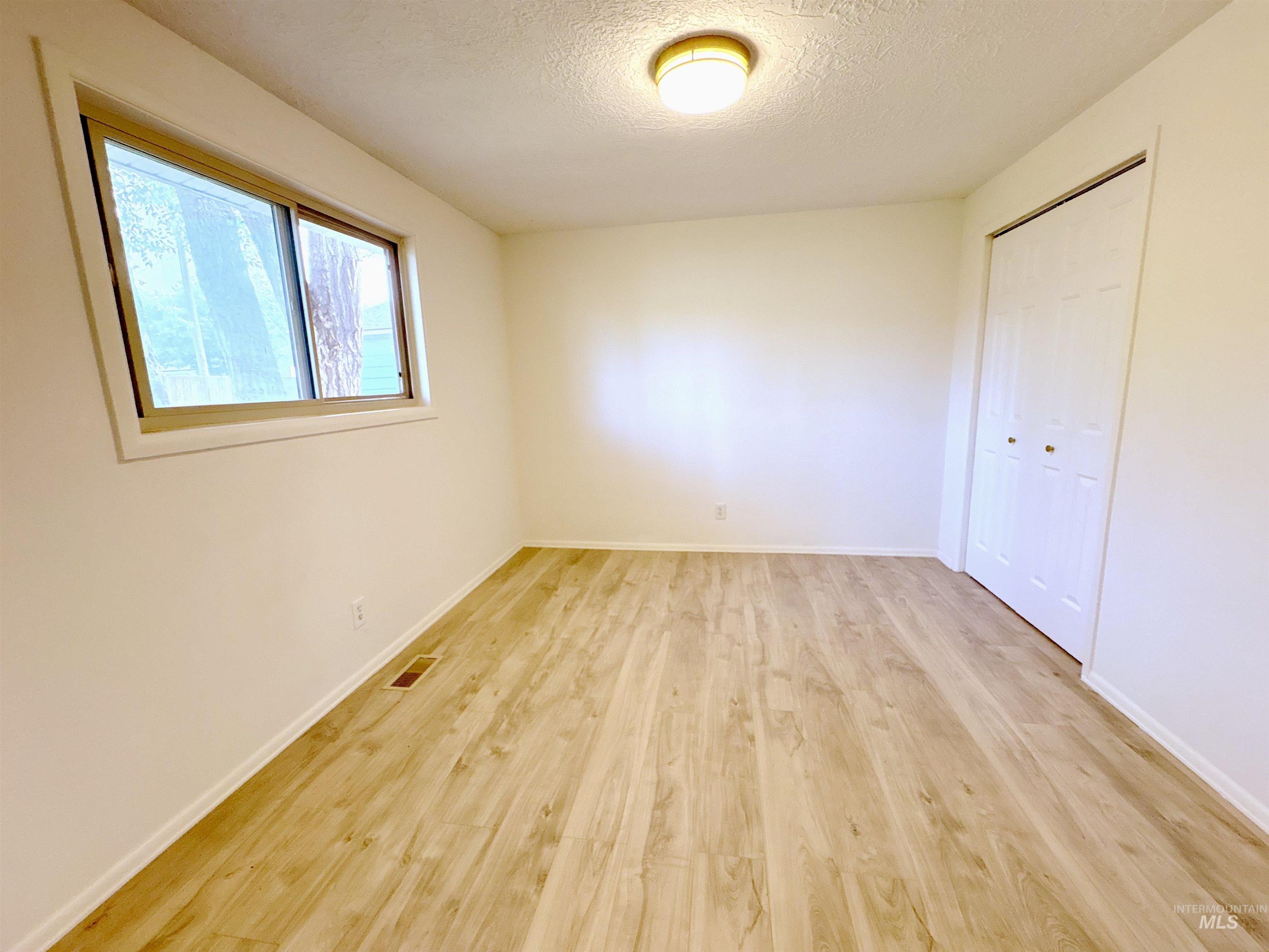 Unfurnished bedroom featuring a textured ceiling, a closet, and light wood finished floors