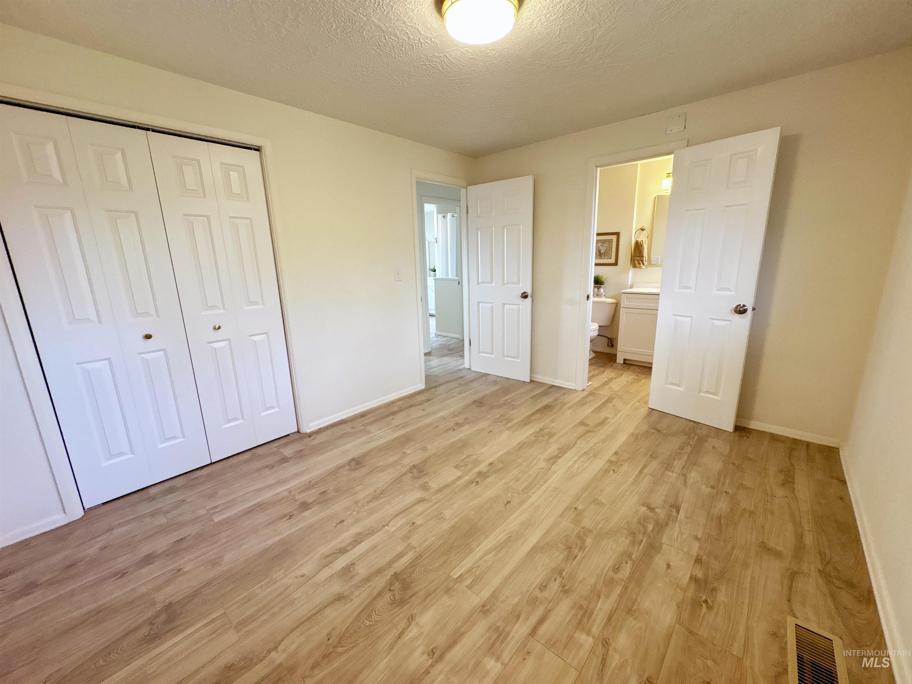 Unfurnished bedroom featuring a textured ceiling, light wood-style floors, a closet, and ensuite bathroom