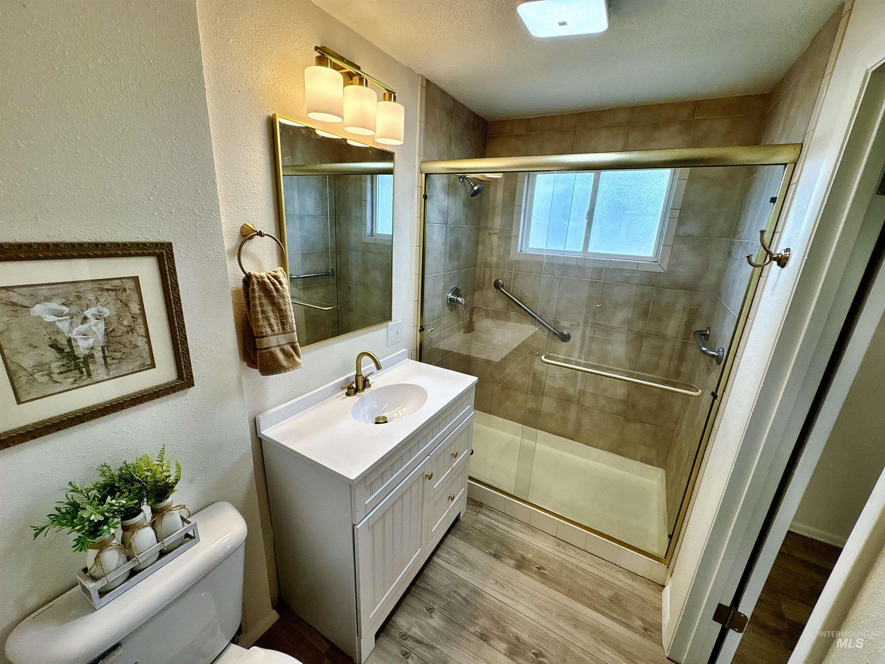 Bathroom featuring a textured wall, light wood-style floors, vanity, a shower stall, and a textured ceiling