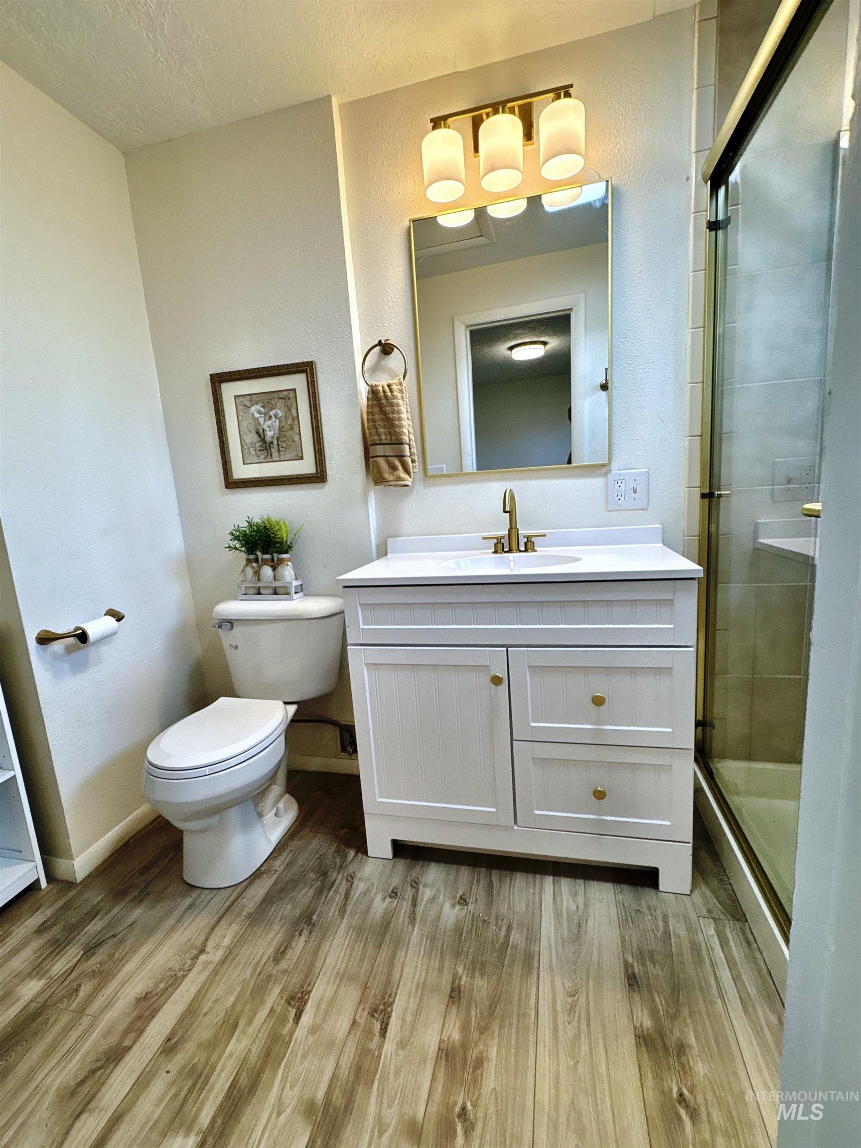 Bathroom with light wood-type flooring, vanity, a shower stall, a textured wall, and a textured ceiling