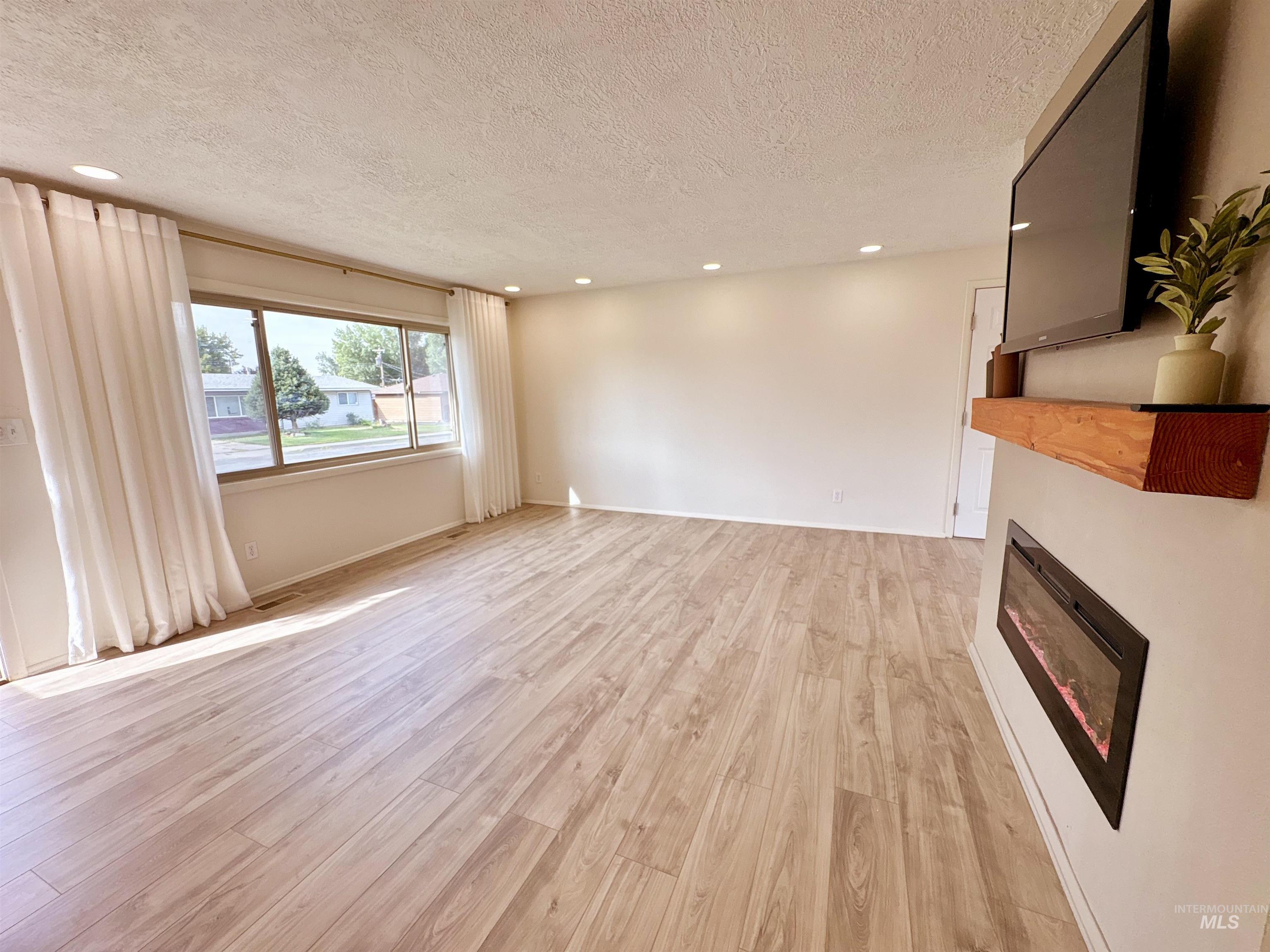 Unfurnished living room featuring a glass covered fireplace, recessed lighting, light wood-style flooring, and a textured ceiling