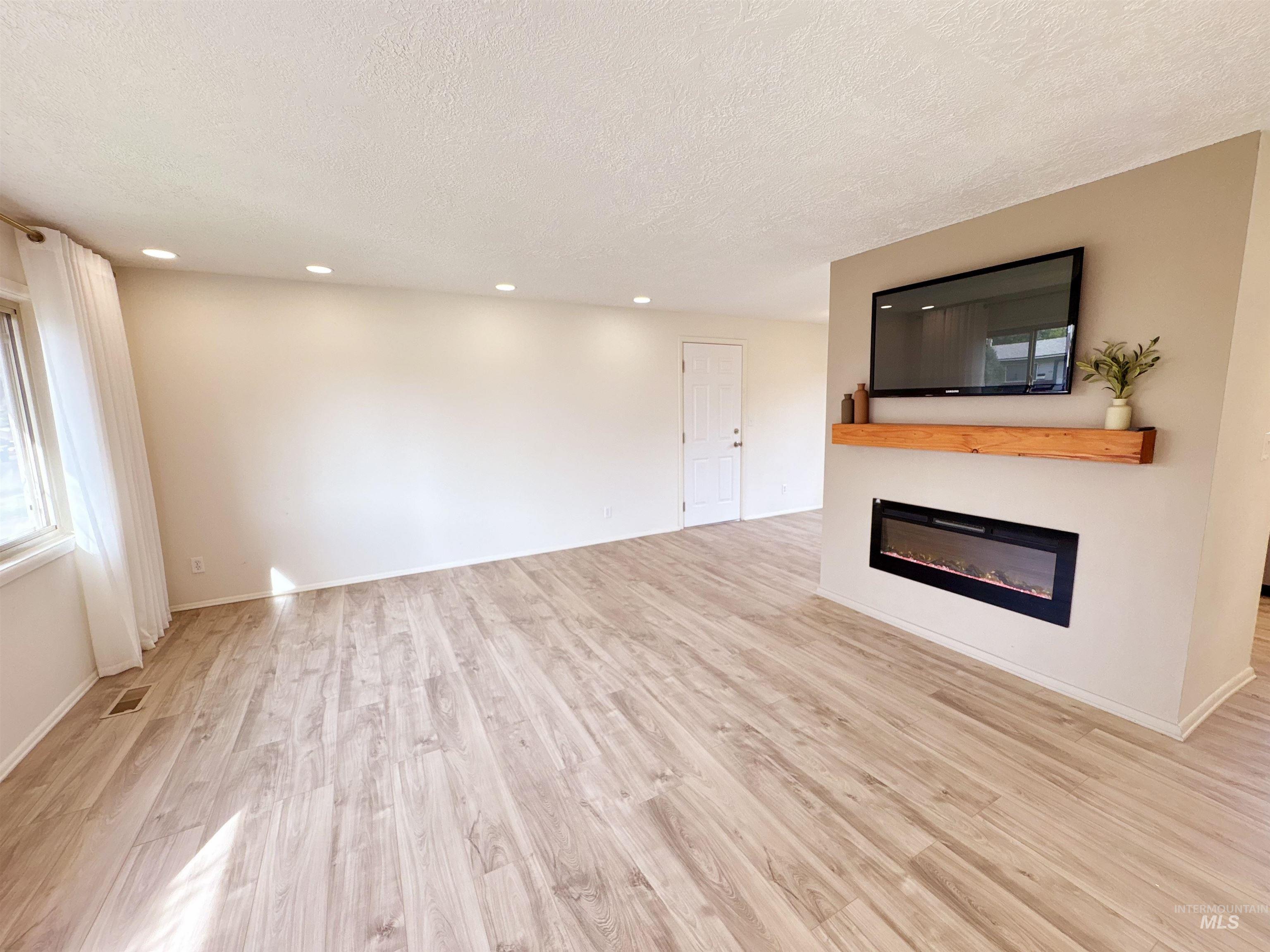 Unfurnished living room with light wood-style flooring, a textured ceiling, a glass covered fireplace, and recessed lighting