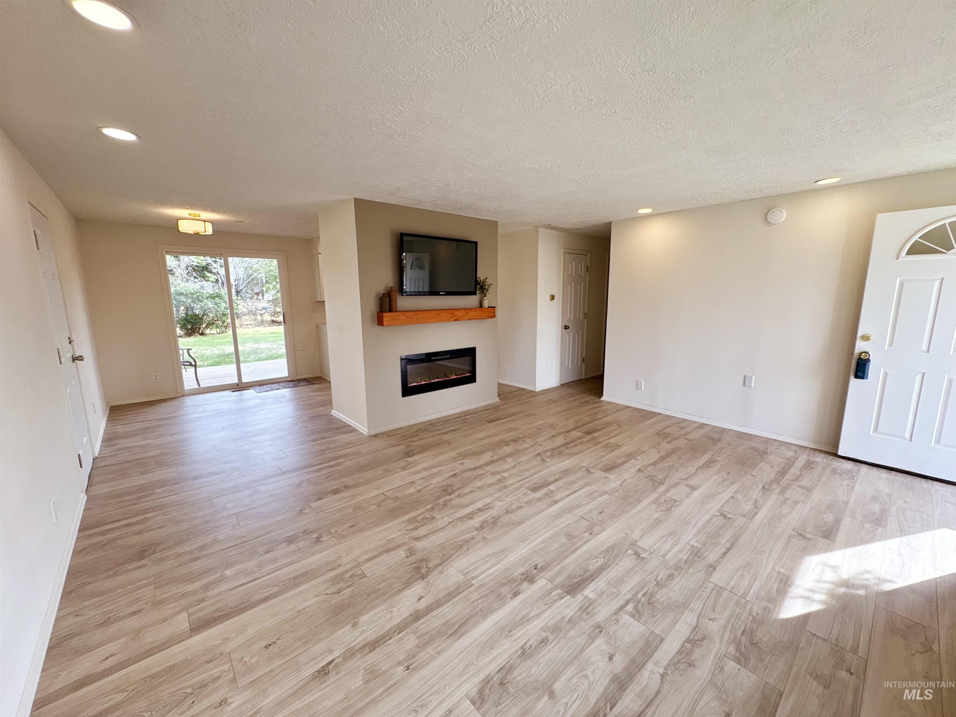 Unfurnished living room with light wood finished floors, recessed lighting, a glass covered fireplace, and a textured ceiling