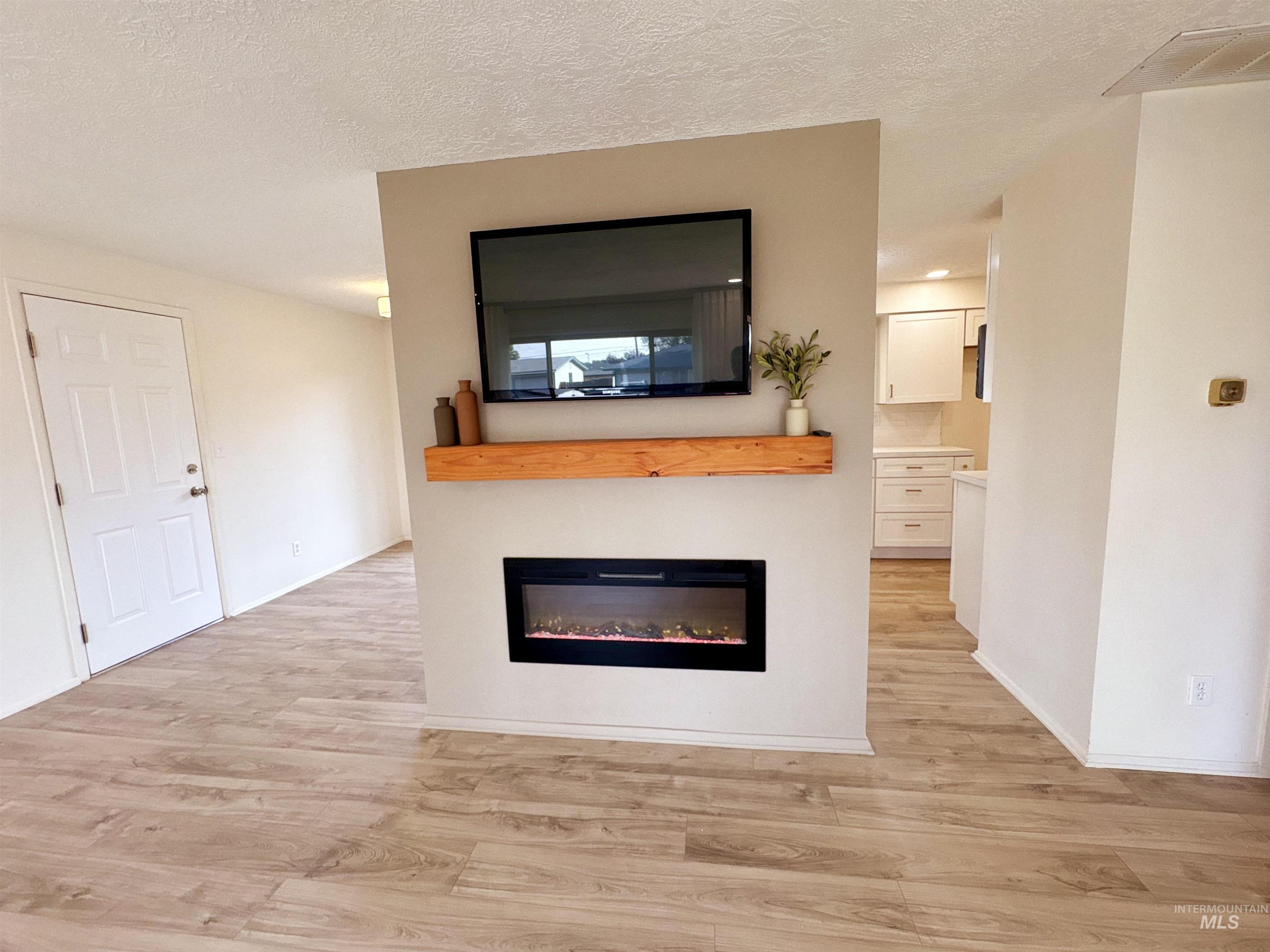 Unfurnished living room with a glass covered fireplace, a textured ceiling, and light wood-type flooring