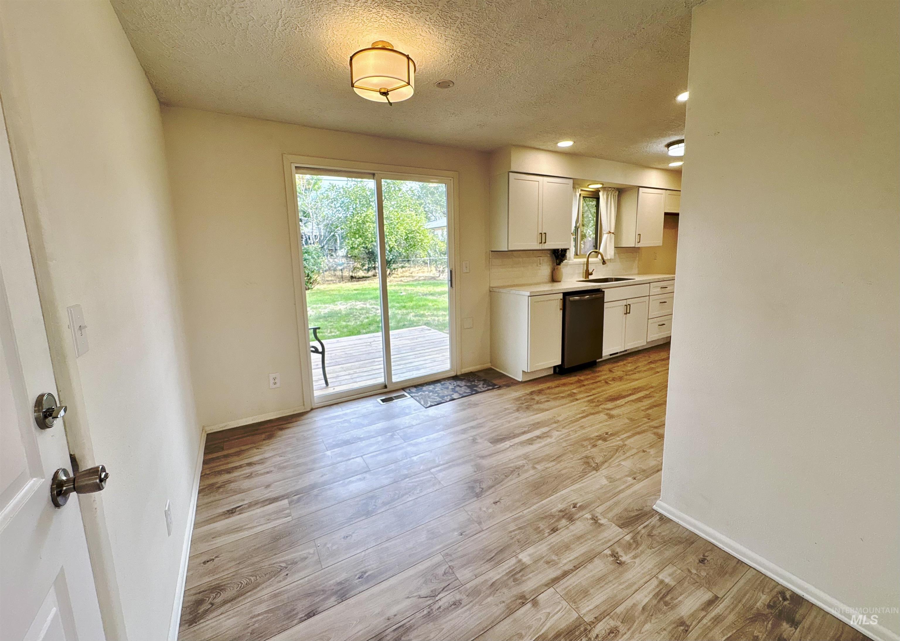 Kitchen featuring white cabinetry, light wood-style flooring, stainless steel dishwasher, a textured ceiling, and backsplash