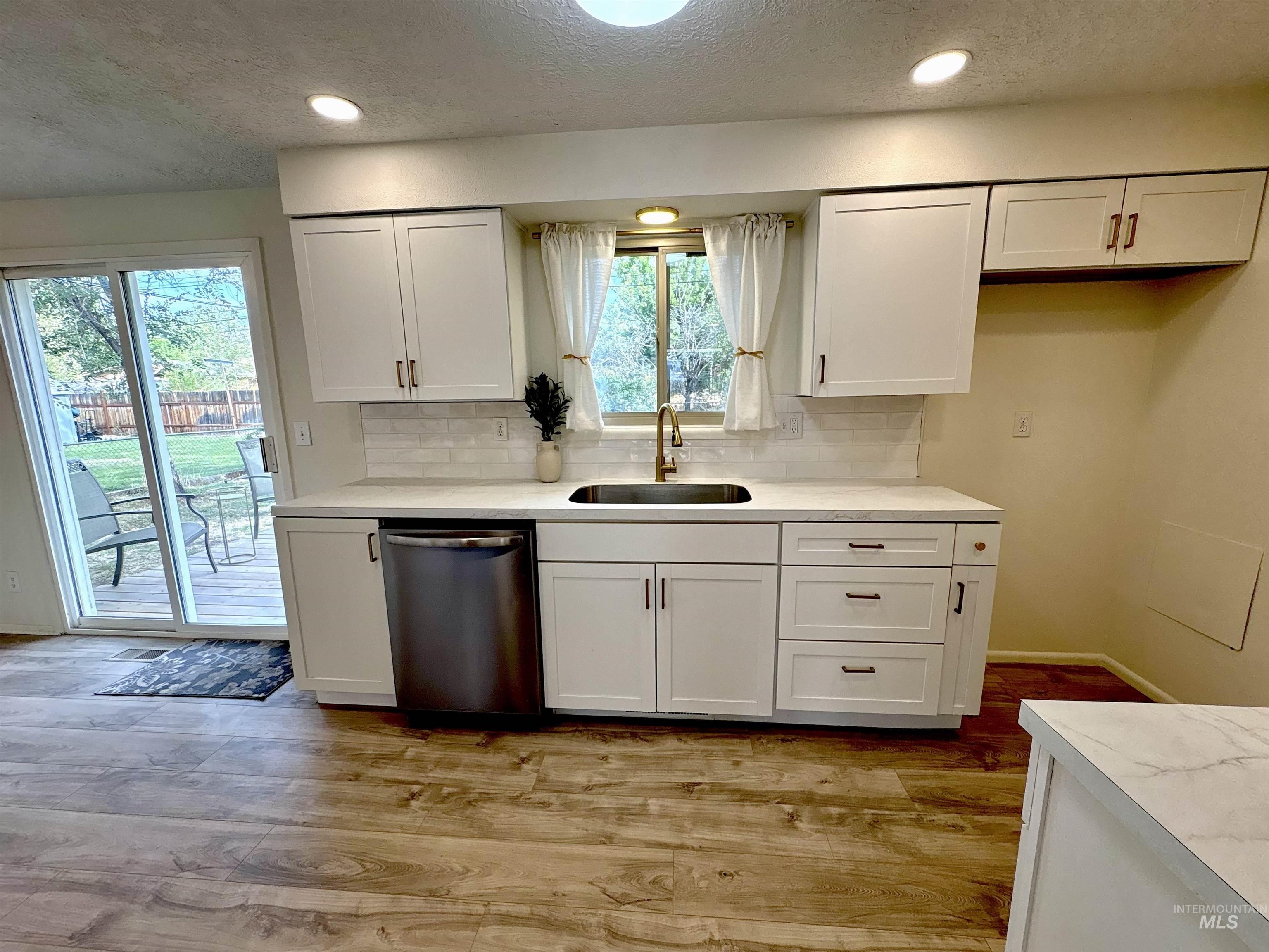 Kitchen featuring a textured ceiling, white cabinetry, dishwasher, decorative backsplash, and light wood-type flooring