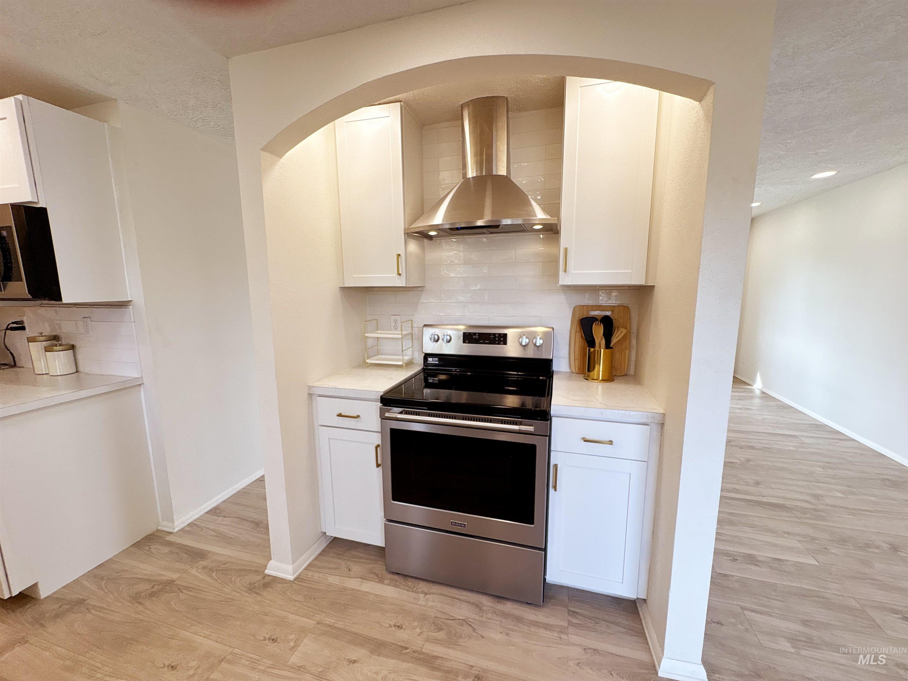 Kitchen featuring stainless steel electric range, wall chimney range hood, tasteful backsplash, light wood-style floors, and a textured ceiling