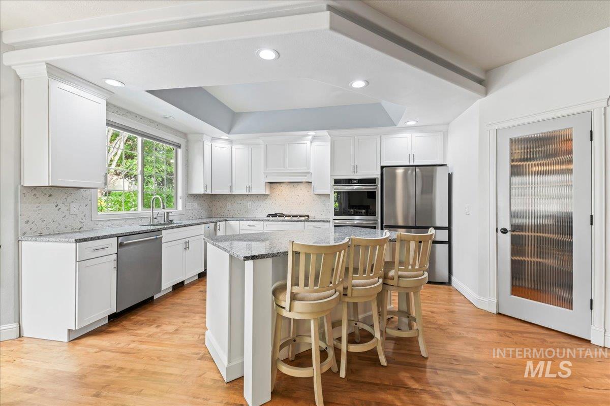 Kitchen featuring light stone countertops, a breakfast bar area, white cabinetry, decorative backsplash, and recessed lighting