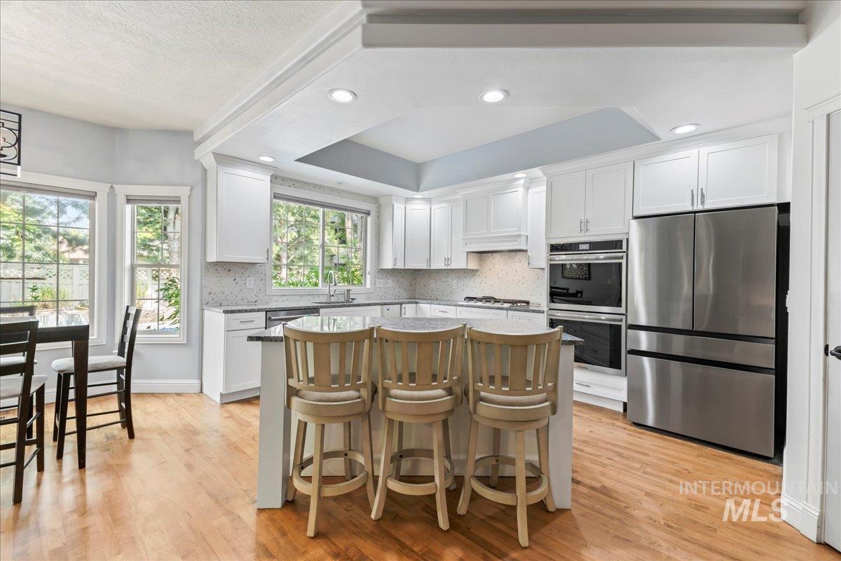 Kitchen with stainless steel appliances, a kitchen breakfast bar, light wood-type flooring, white cabinets, and recessed lighting