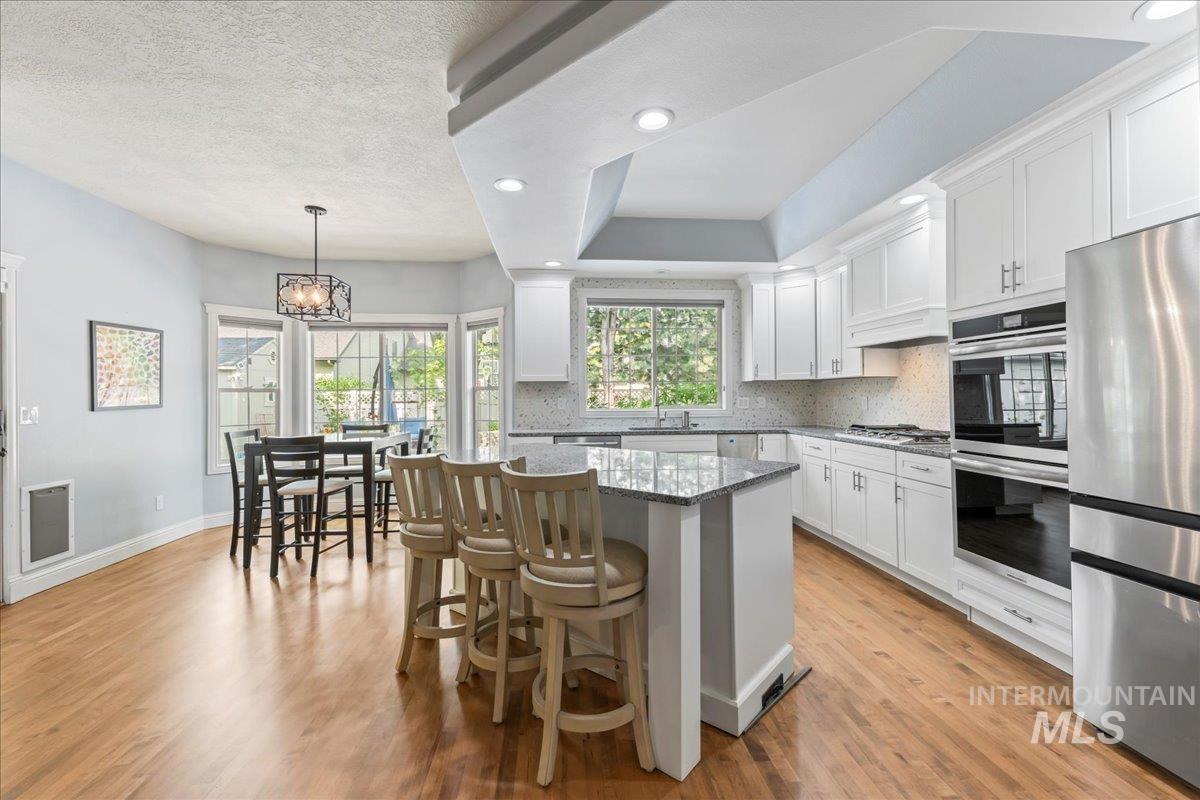 Kitchen featuring dark stone counters, a kitchen breakfast bar, decorative light fixtures, stainless steel appliances, and light wood-type flooring