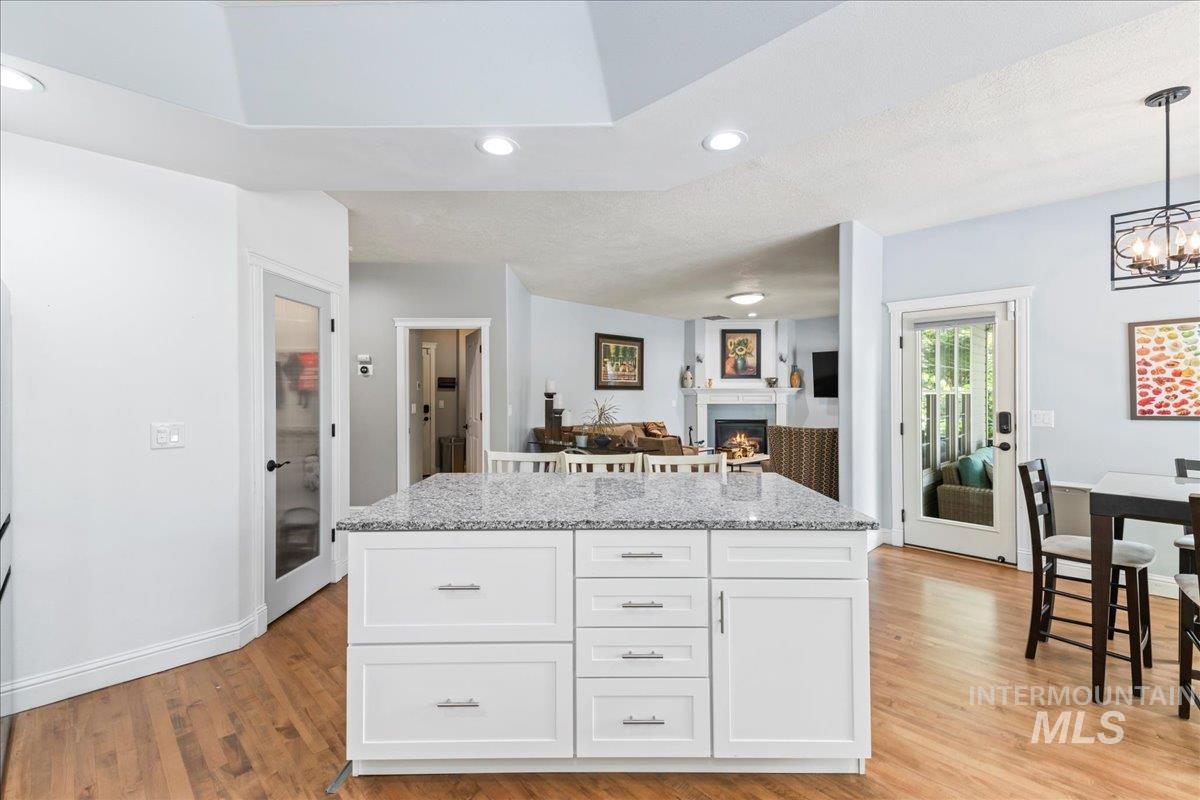 Kitchen featuring recessed lighting, a warm lit fireplace, white cabinetry, a center island, and light stone counters