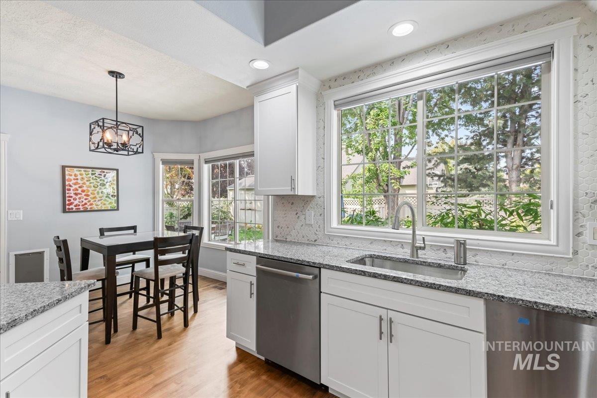 Kitchen with light stone countertops, light wood-style flooring, recessed lighting, pendant lighting, and dishwasher