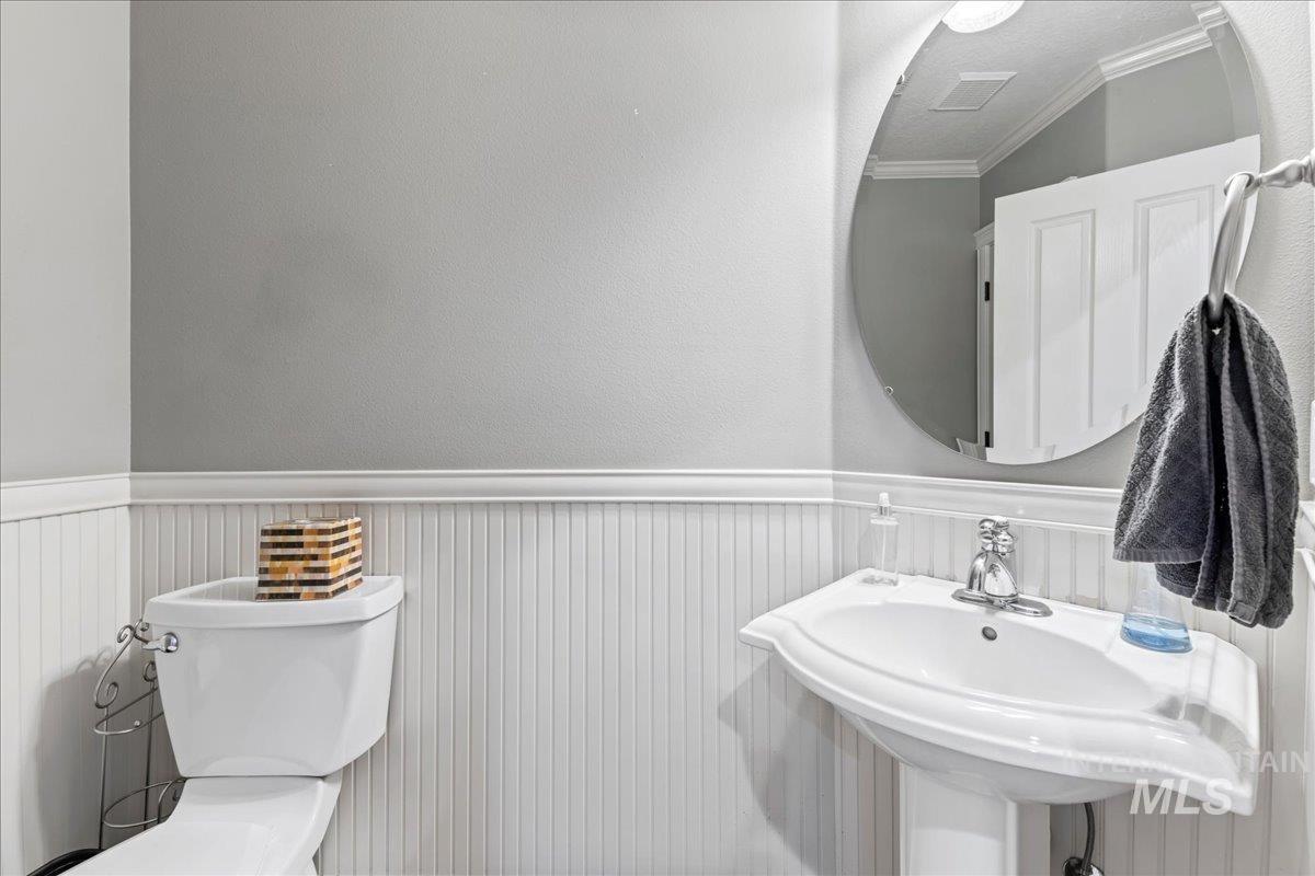 Bathroom featuring a wainscoted wall, crown molding, and a textured wall