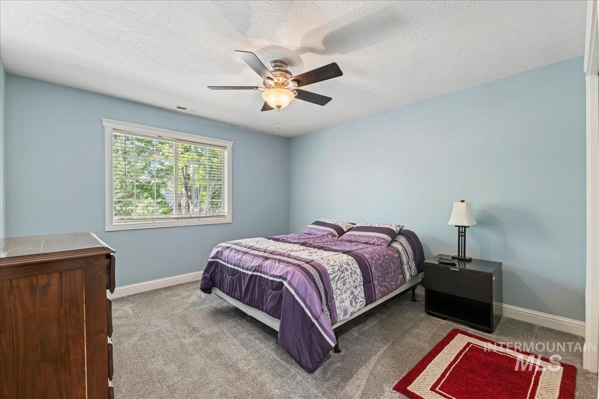 Carpeted bedroom featuring ceiling fan and a textured ceiling