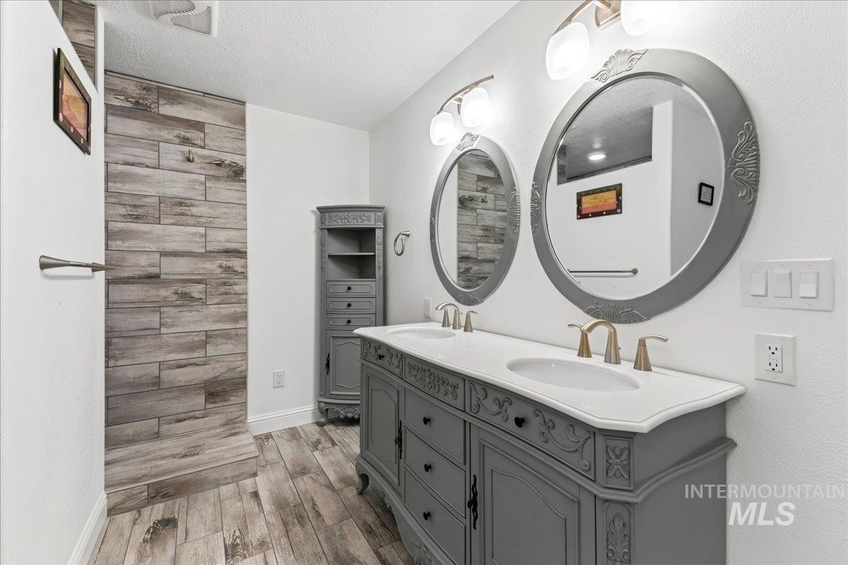 Full bathroom featuring light wood-style flooring, a textured ceiling, and double vanity
