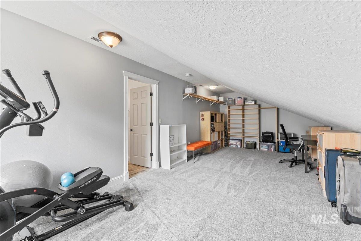 Workout area with lofted ceiling, a textured ceiling, and light carpet