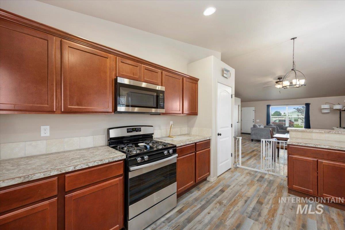 Kitchen with appliances with stainless steel finishes, light wood-type flooring, a chandelier, hanging light fixtures, and light countertops