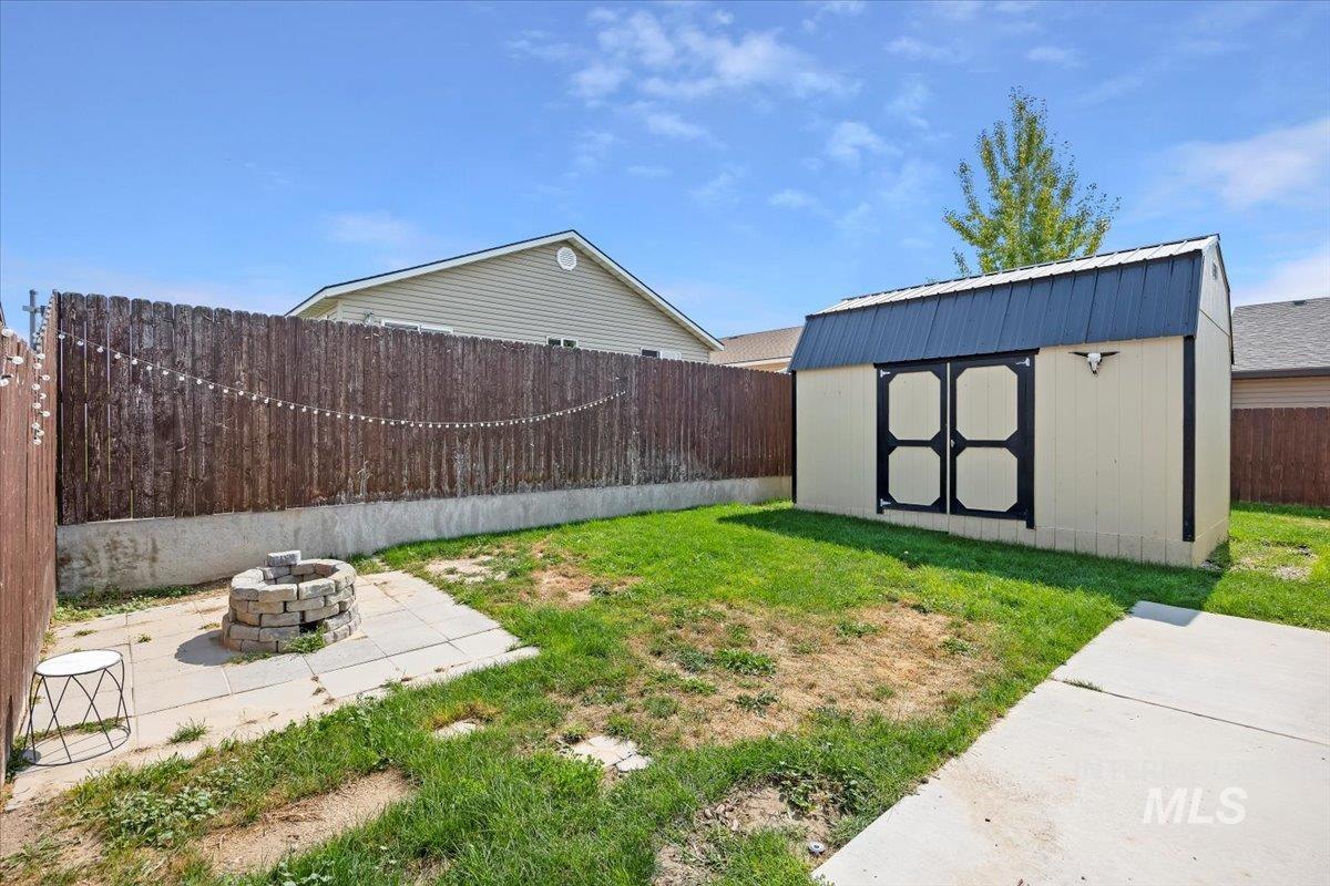 Fenced backyard with a storage shed, an outdoor fire pit, and a patio area
