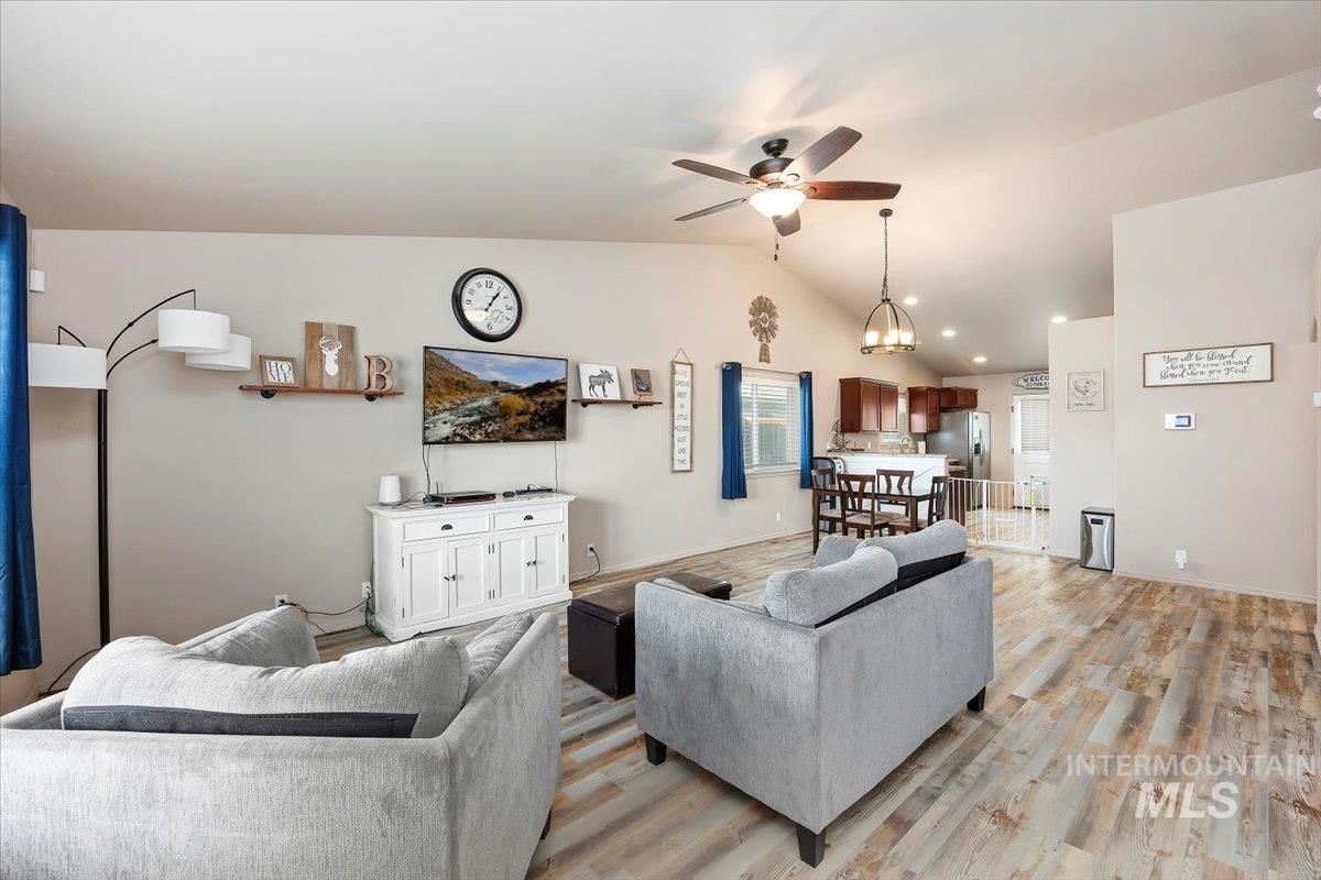 Living room with a ceiling fan, light wood-type flooring, and vaulted ceiling