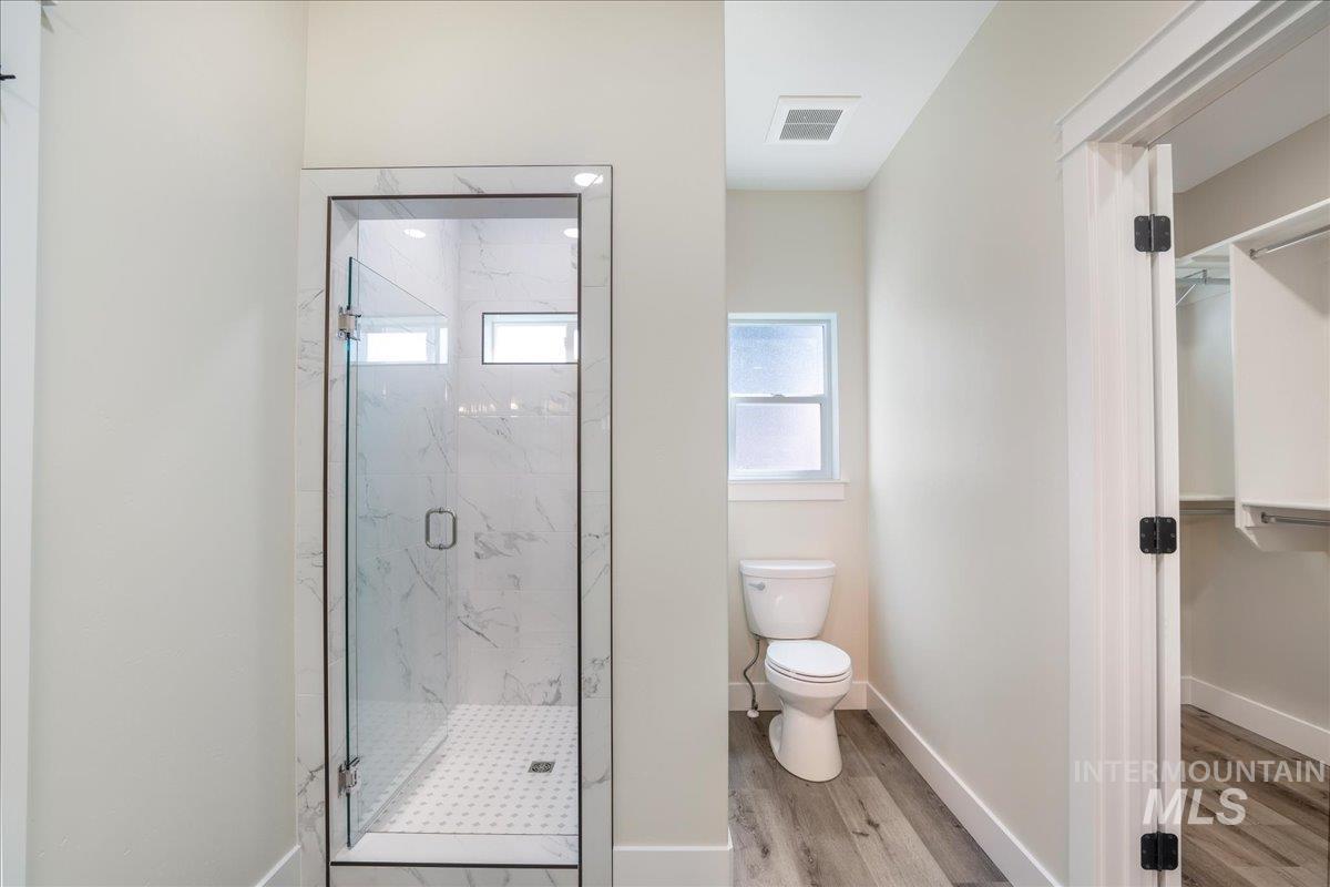 Bathroom featuring a marble finish shower, light wood-style floors, and a spacious closet