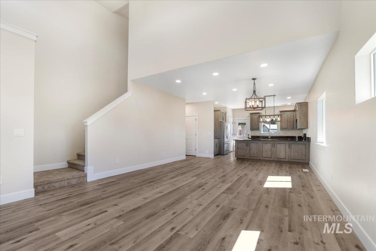 Unfurnished living room featuring stairway, recessed lighting, light wood-style floors, a high ceiling, and a chandelier