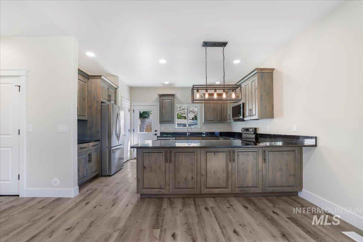 Kitchen with a peninsula, stainless steel appliances, pendant lighting, light wood-style floors, and dark stone countertops
