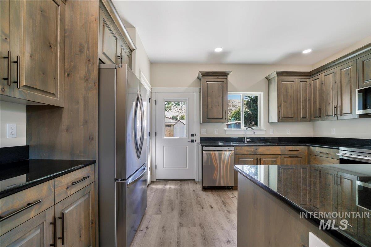 Kitchen with appliances with stainless steel finishes, light wood-type flooring, dark stone countertops, and recessed lighting