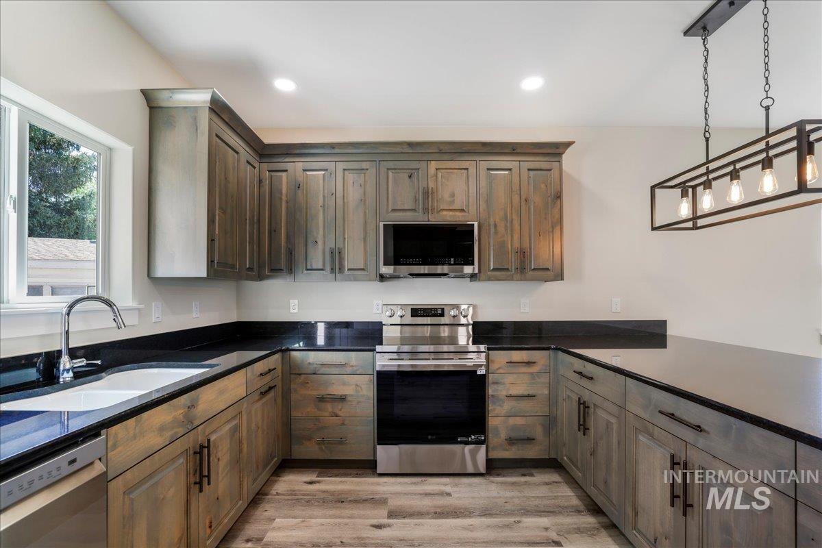 Kitchen featuring appliances with stainless steel finishes, decorative light fixtures, light wood-type flooring, dark stone counters, and recessed lighting