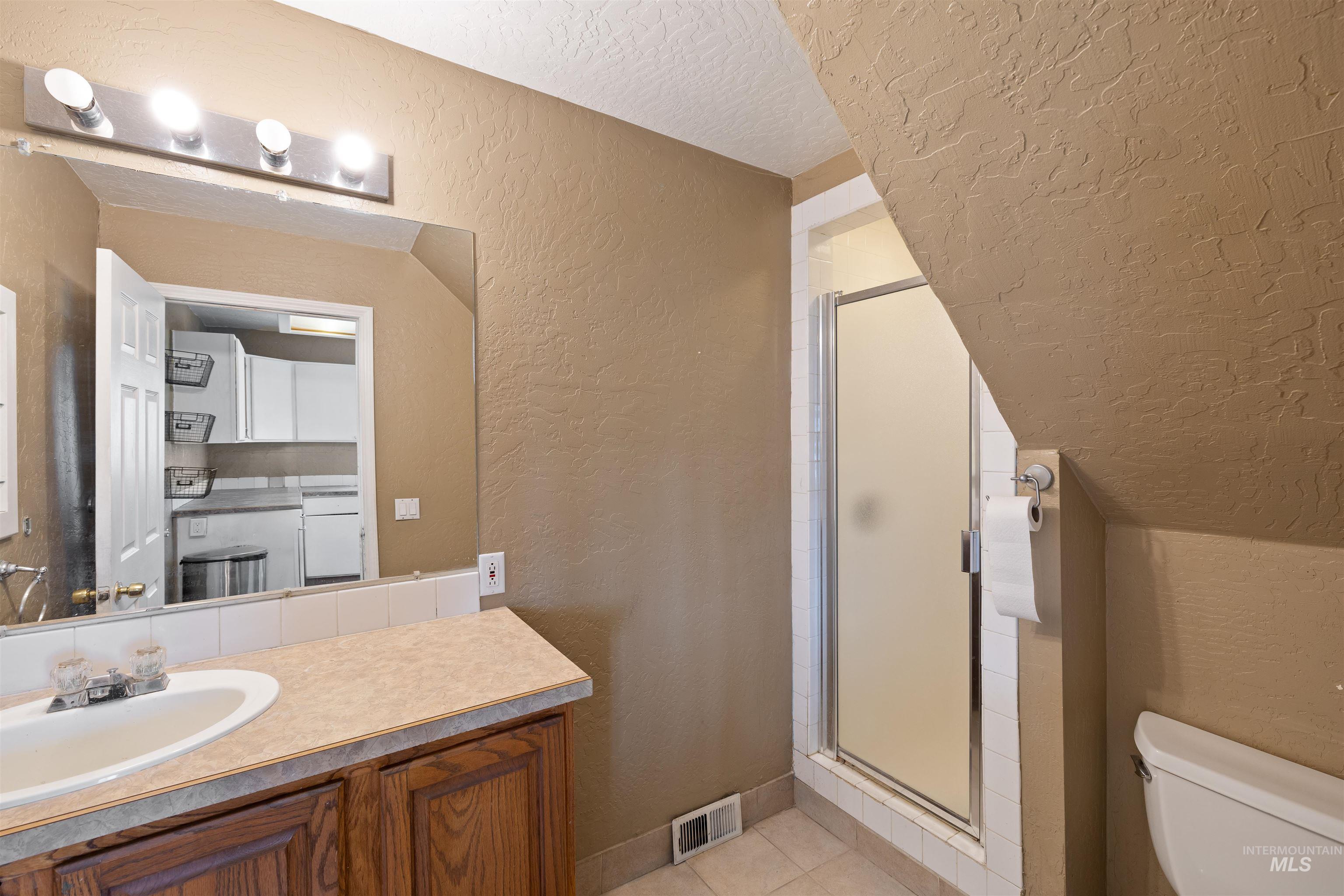 Full bath featuring a textured wall, a textured ceiling, a stall shower, vanity, and light tile patterned flooring