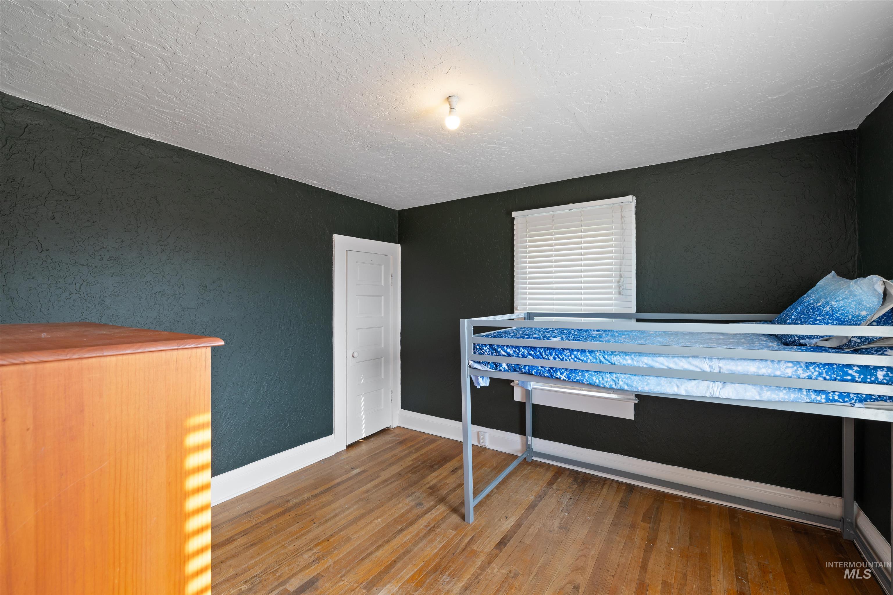 Bedroom featuring a textured wall, light wood-style floors, and a textured ceiling