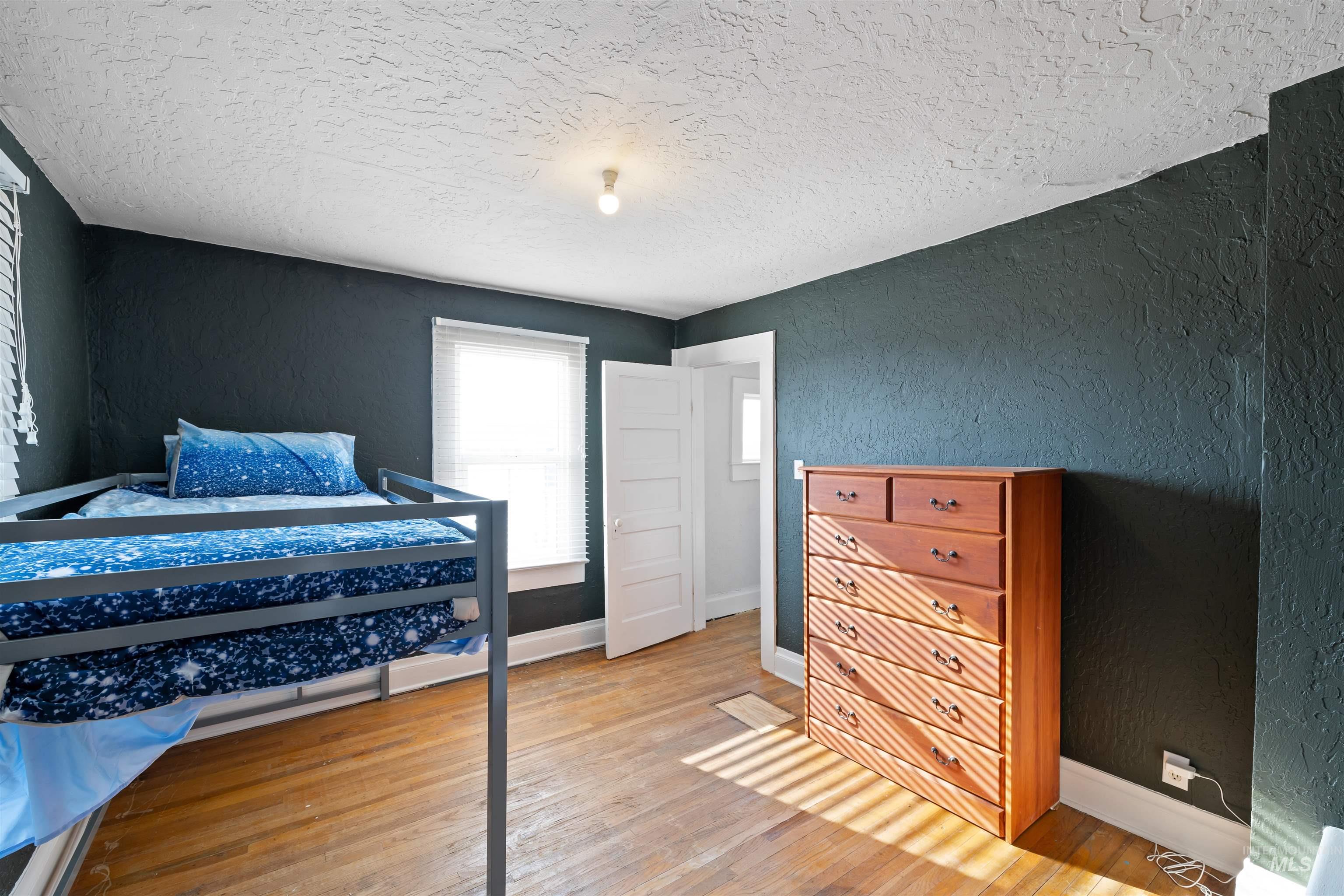 Bedroom with a textured wall, light wood-style flooring, and a textured ceiling