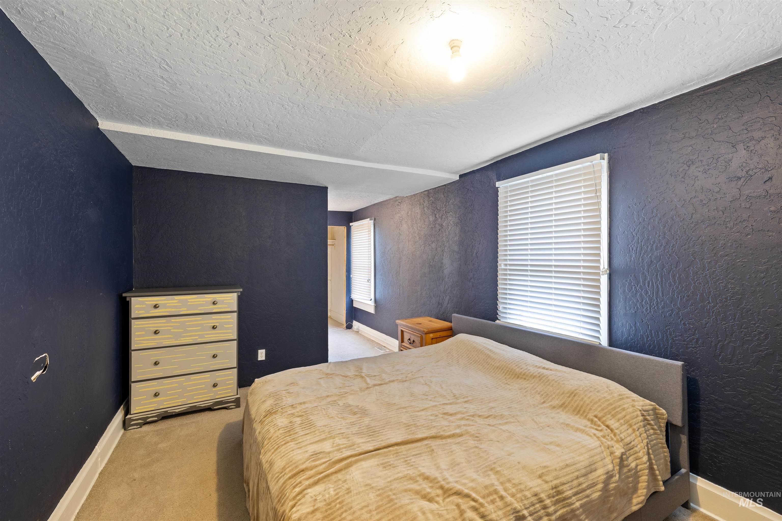 Bedroom with a textured wall, light colored carpet, and a textured ceiling