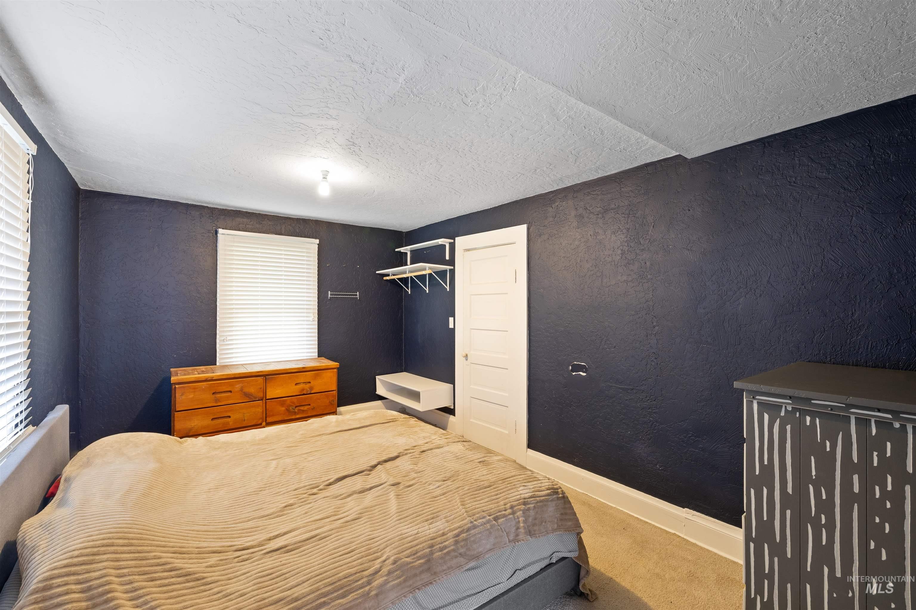 Carpeted bedroom with a textured wall, a textured ceiling, and multiple windows