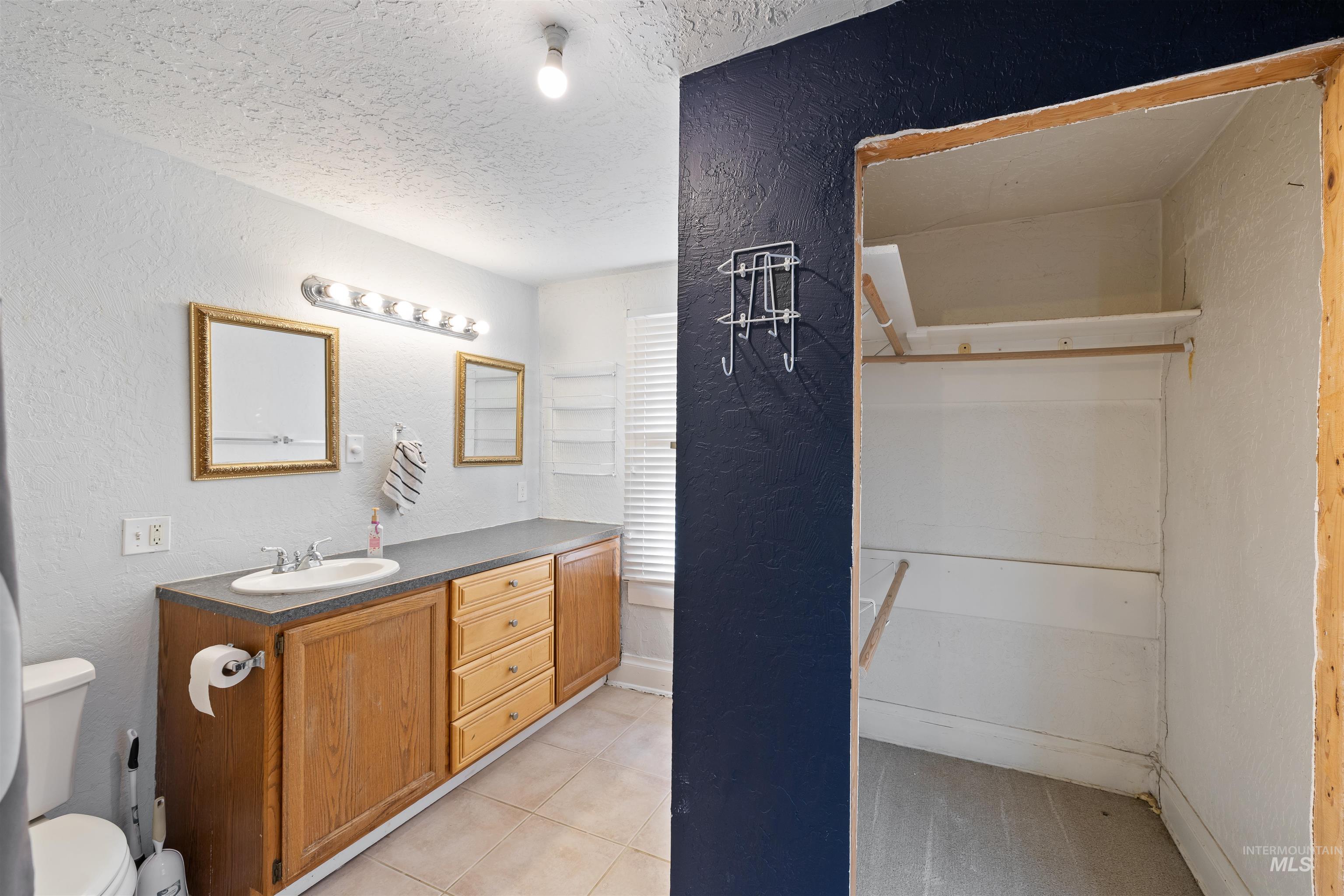 Bathroom featuring a textured wall, vanity, a textured ceiling, and light tile patterned flooring