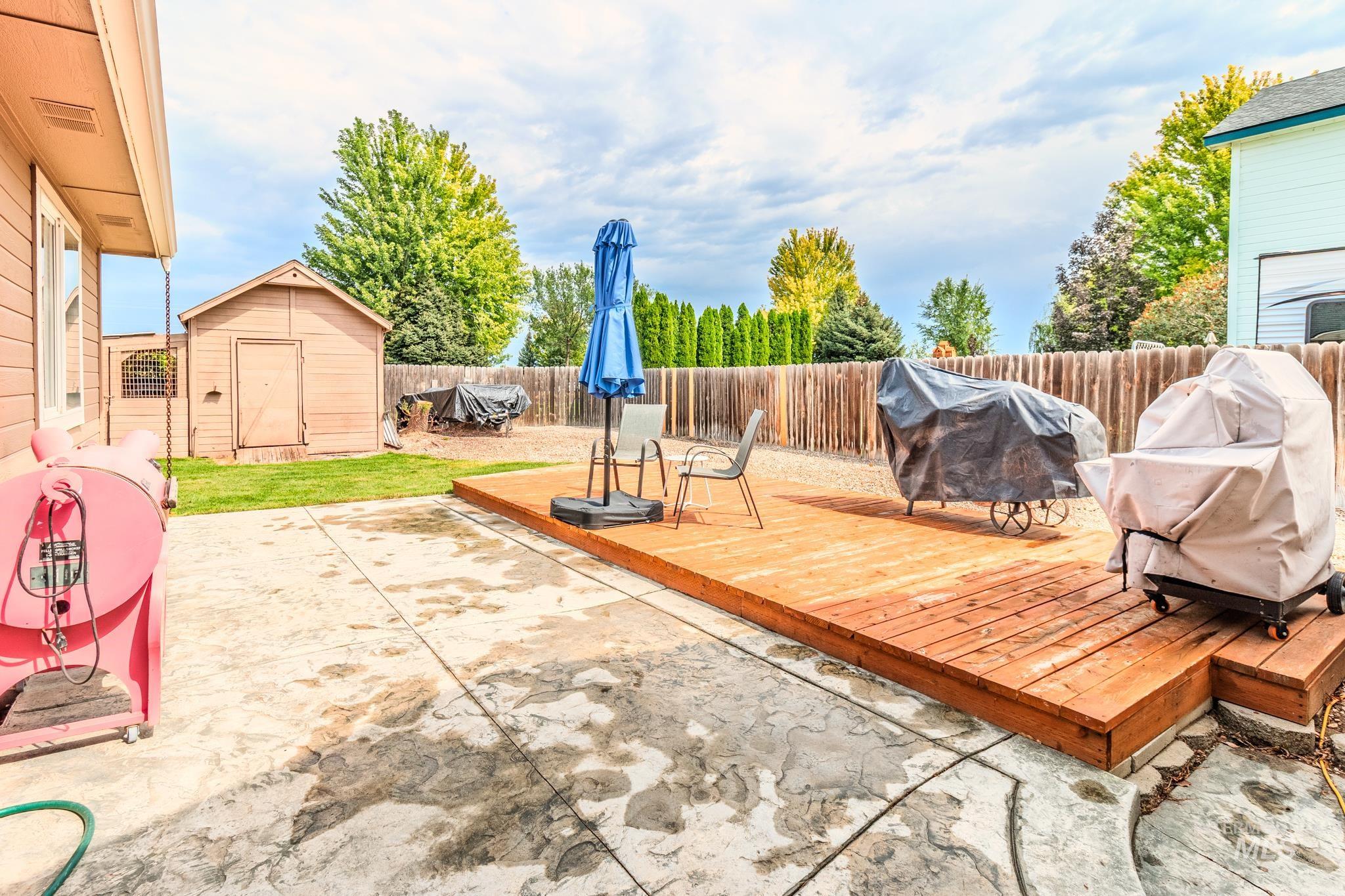 Fenced backyard with a grill, a wooden deck, a shed, and a patio
