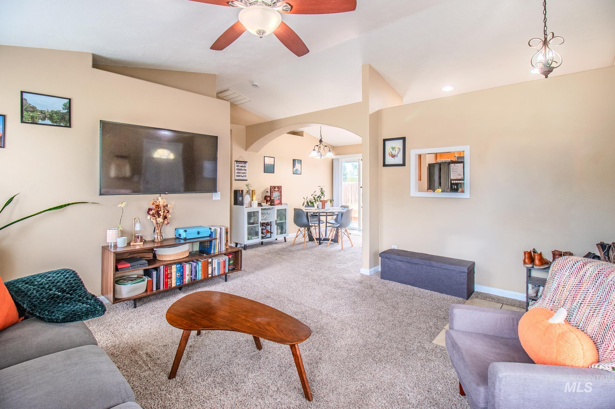 Carpeted living area with lofted ceiling, arched walkways, and a ceiling fan