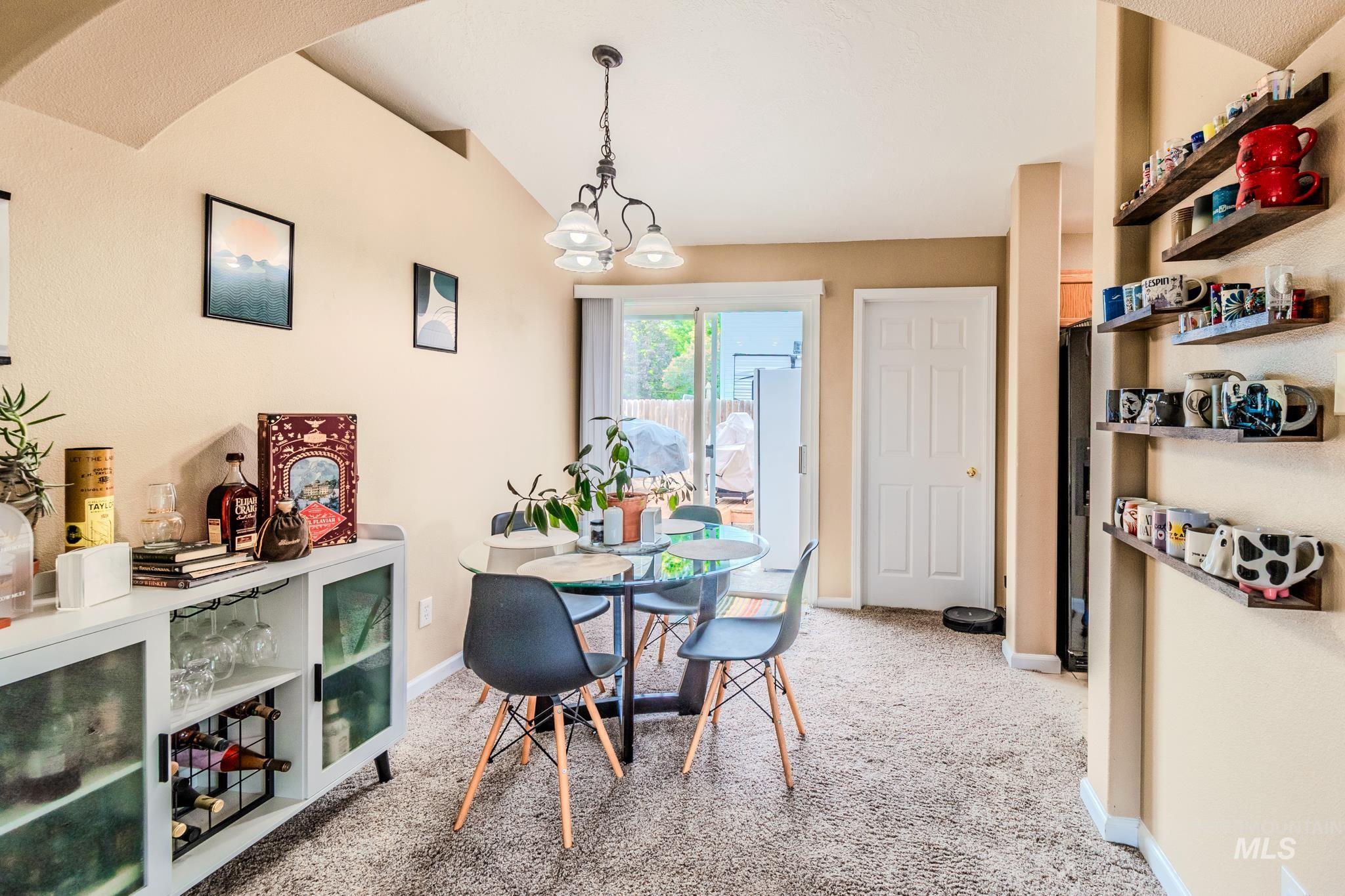 Dining area with light colored carpet, a chandelier, and vaulted ceiling