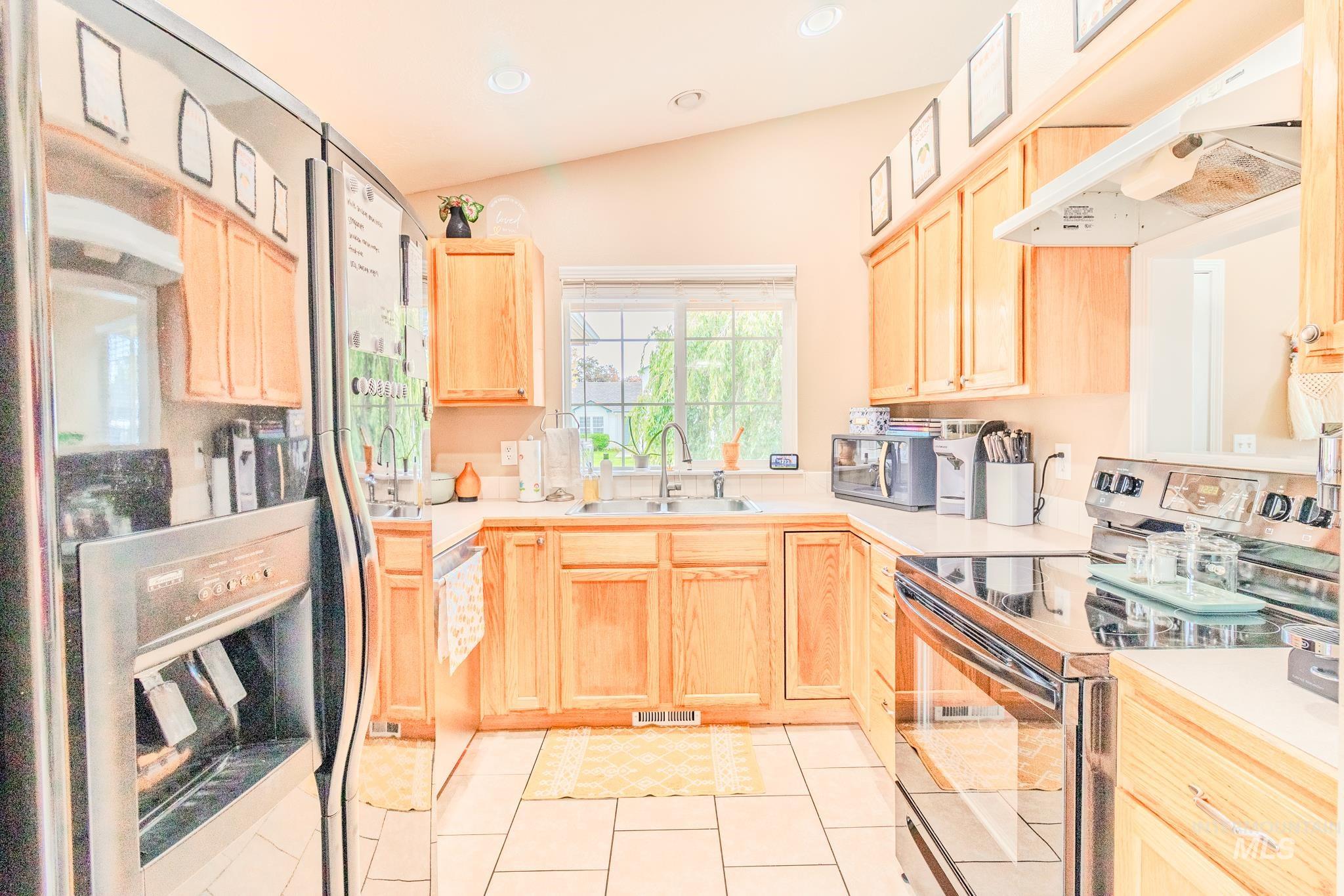 Kitchen featuring light brown cabinets, appliances with stainless steel finishes, light countertops, recessed lighting, and lofted ceiling