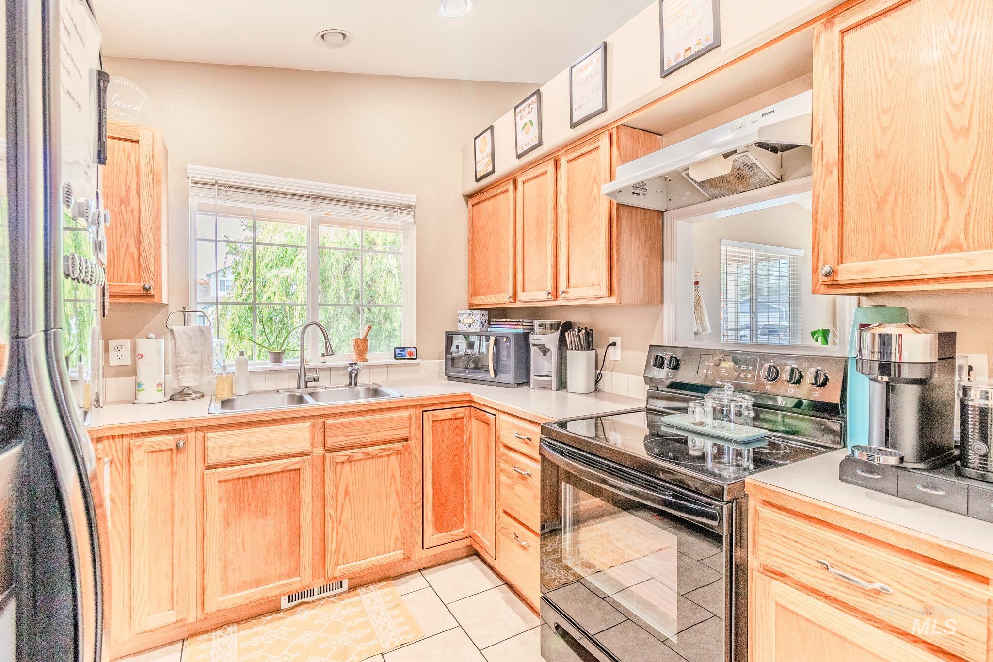 Kitchen with appliances with stainless steel finishes, light brown cabinetry, under cabinet range hood, light countertops, and light tile patterned flooring