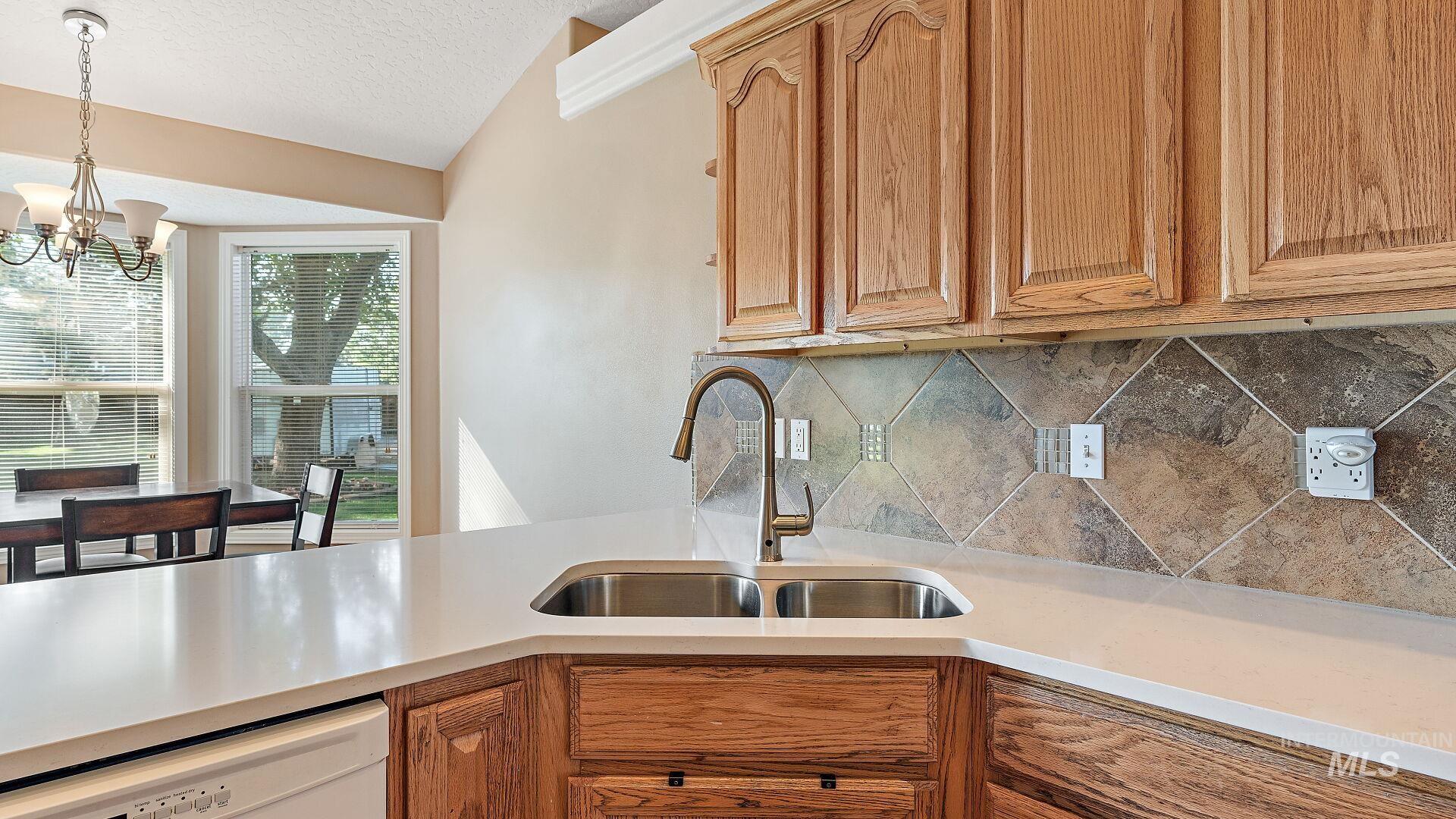 Kitchen featuring dishwasher, brown cabinetry, decorative light fixtures, lofted ceiling, and a textured ceiling