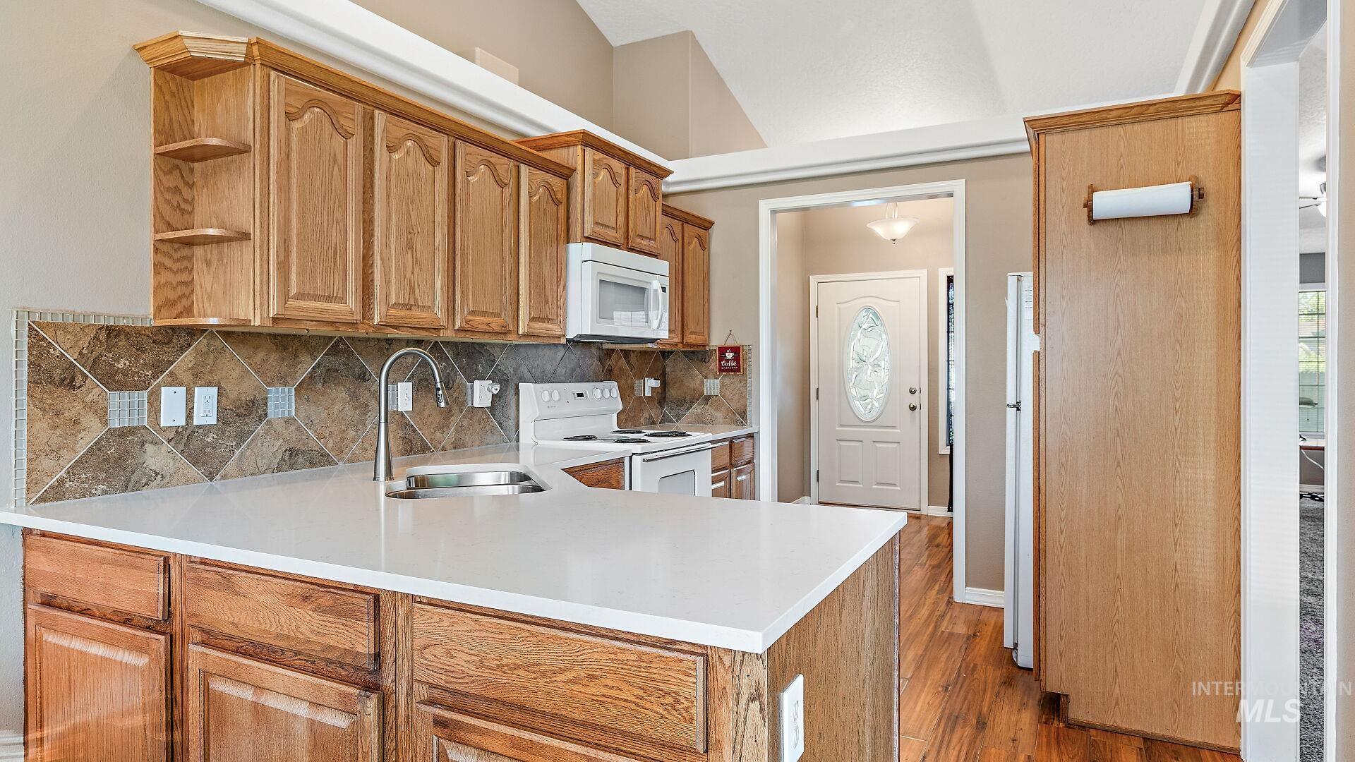 Kitchen with white appliances, wood finished floors, open shelves, backsplash, and brown cabinetry