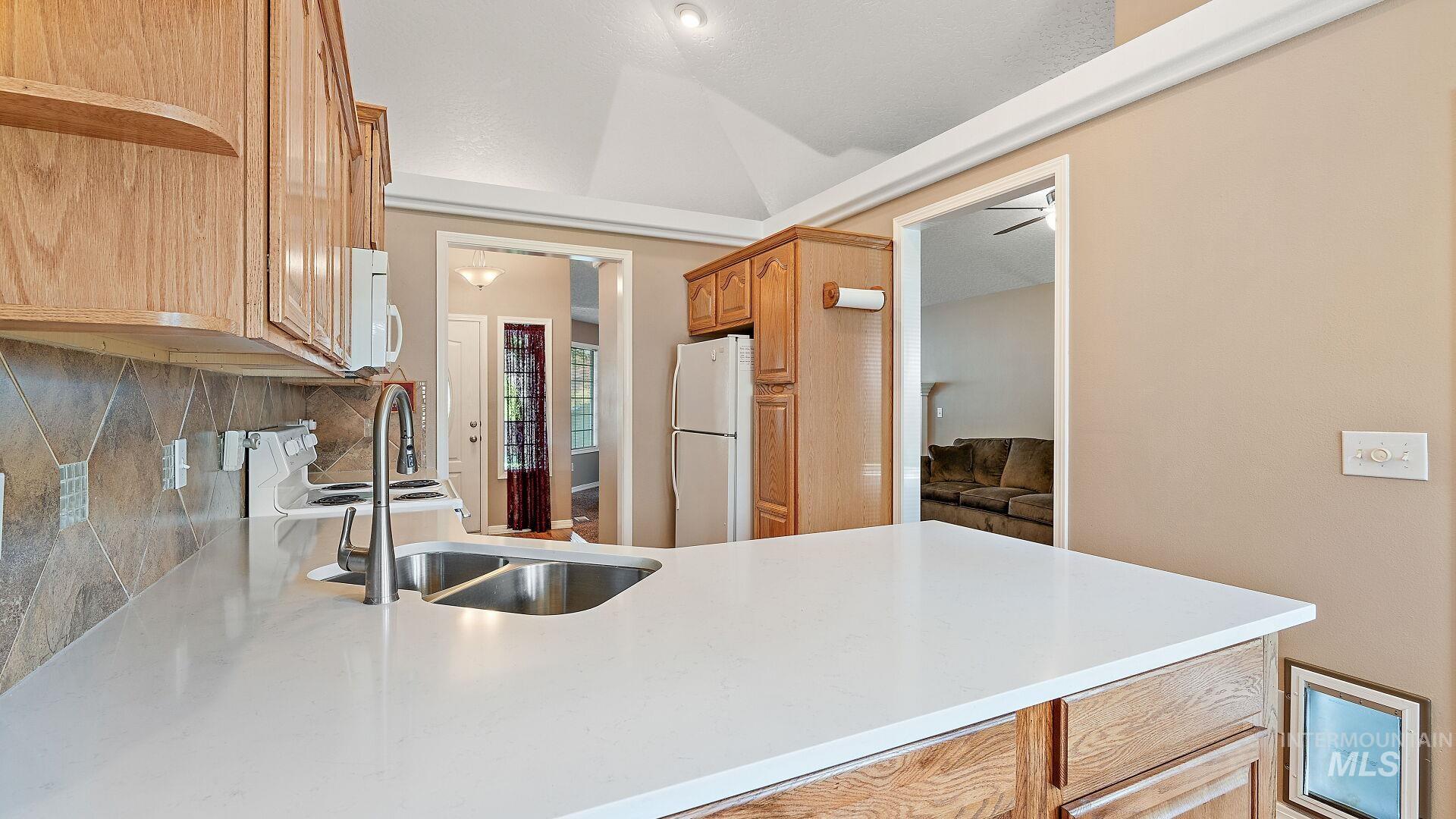 Kitchen featuring white appliances, light stone counters, tasteful backsplash, open shelves, and a peninsula