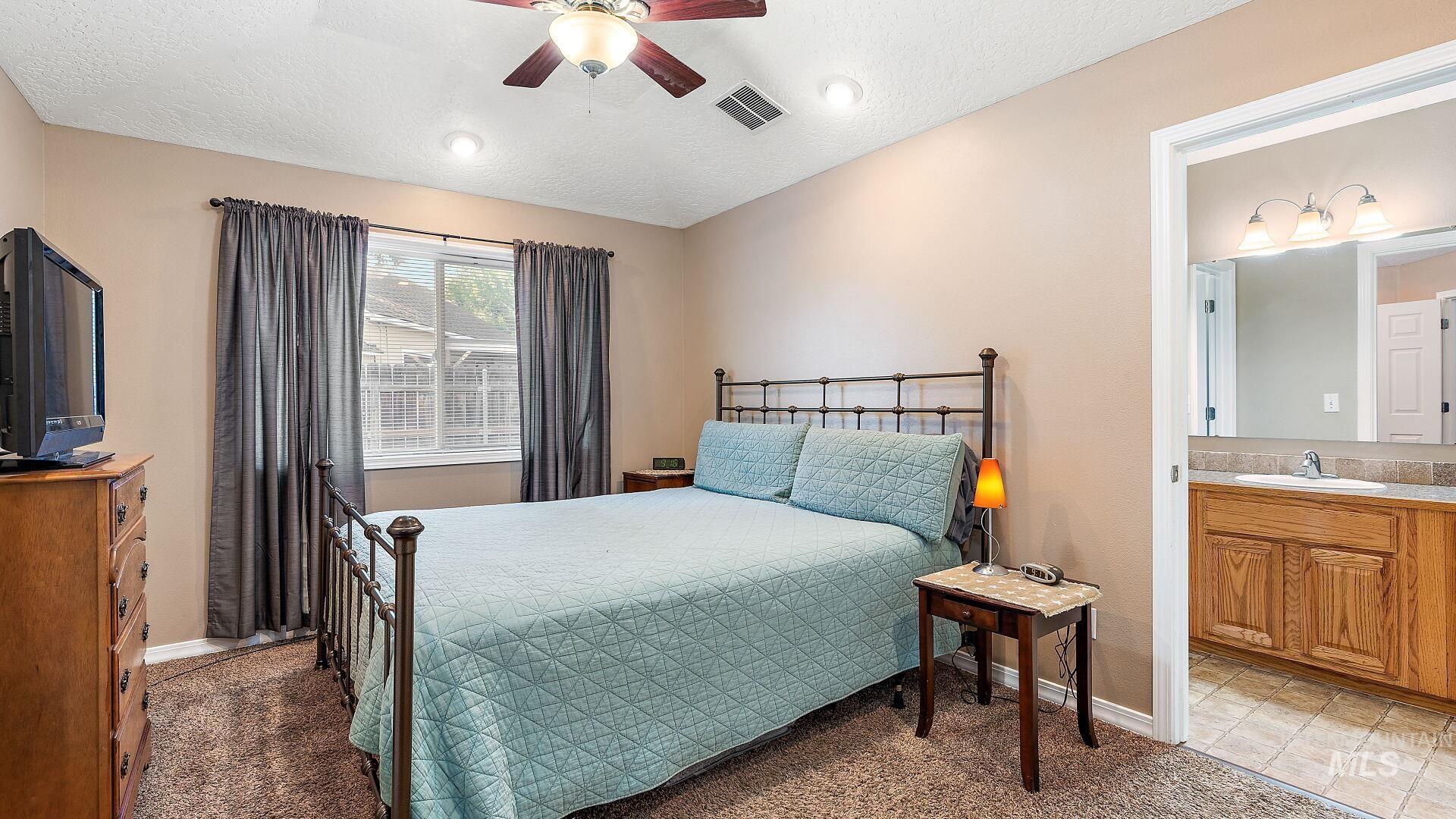 Carpeted bedroom featuring ceiling fan, a textured ceiling, and connected bathroom