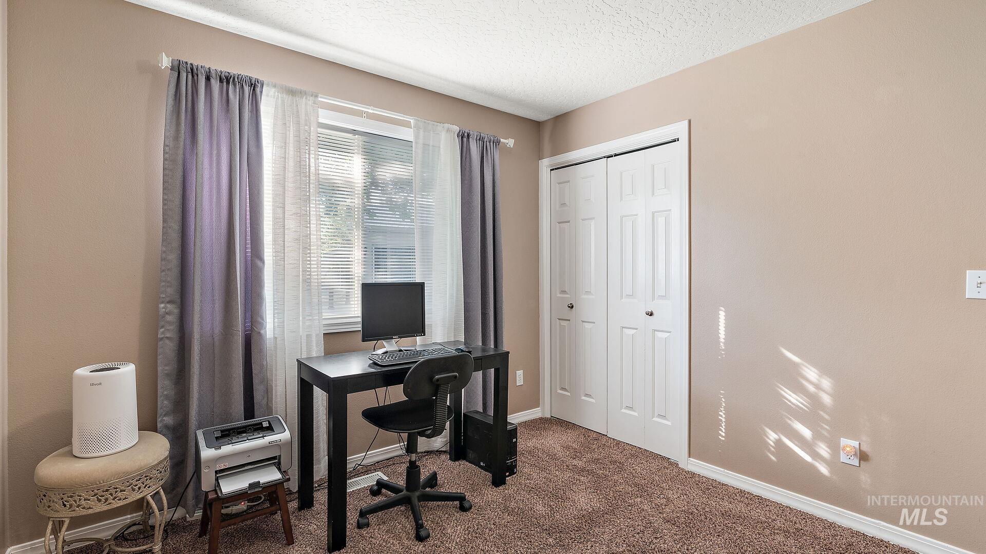 Carpeted office space with a textured ceiling and baseboards